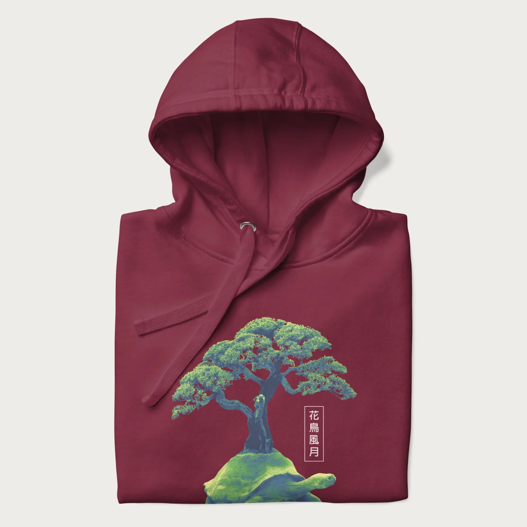 Folded maroon hoodie with a vibrant graphic of a turtle carrying a bonsai tree and Japanese text '花鳥風月.'