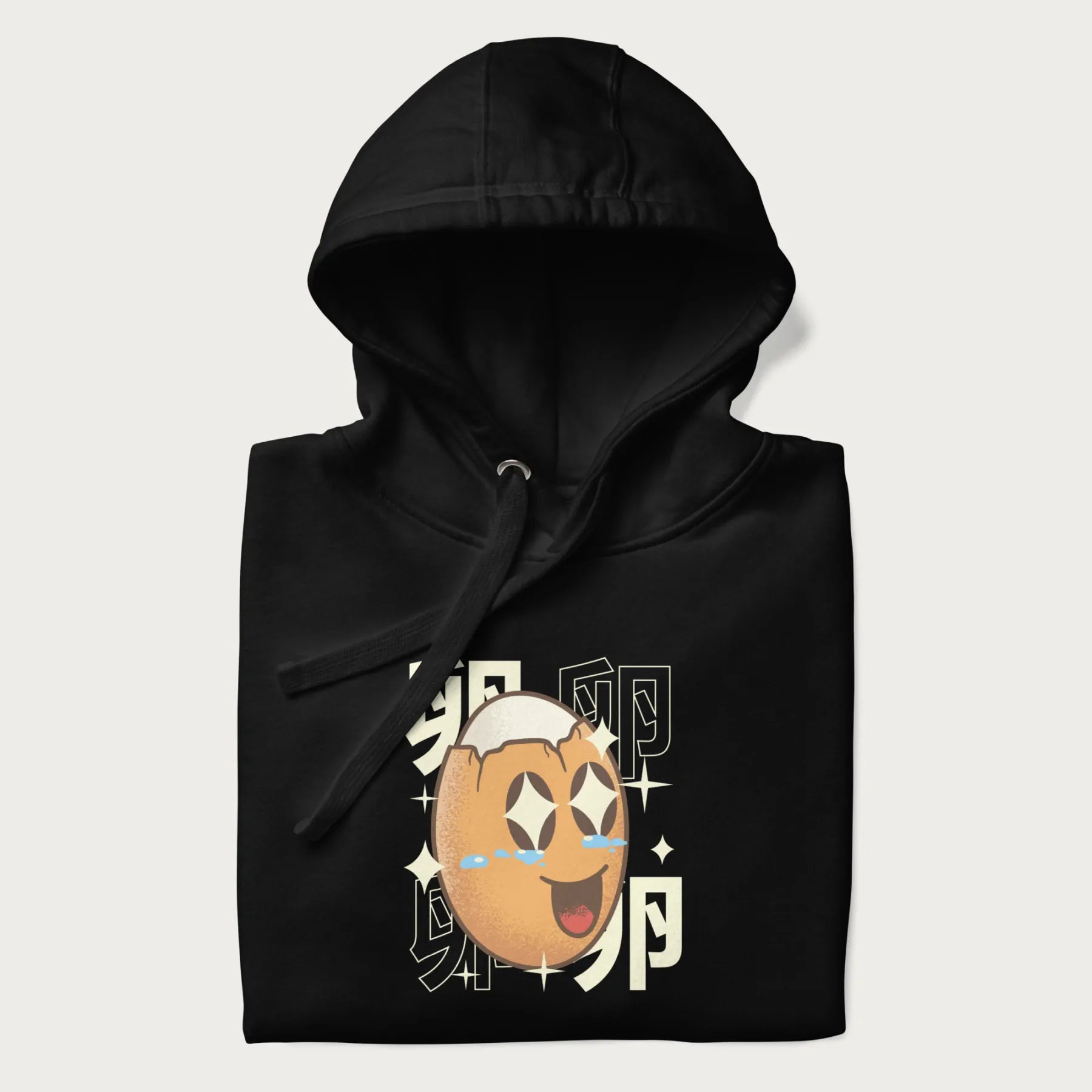 Folded black hoodie with Japanese graphic of a smiling egg with tears of joy, surrounded by the Japanese text '卵' (Egg).