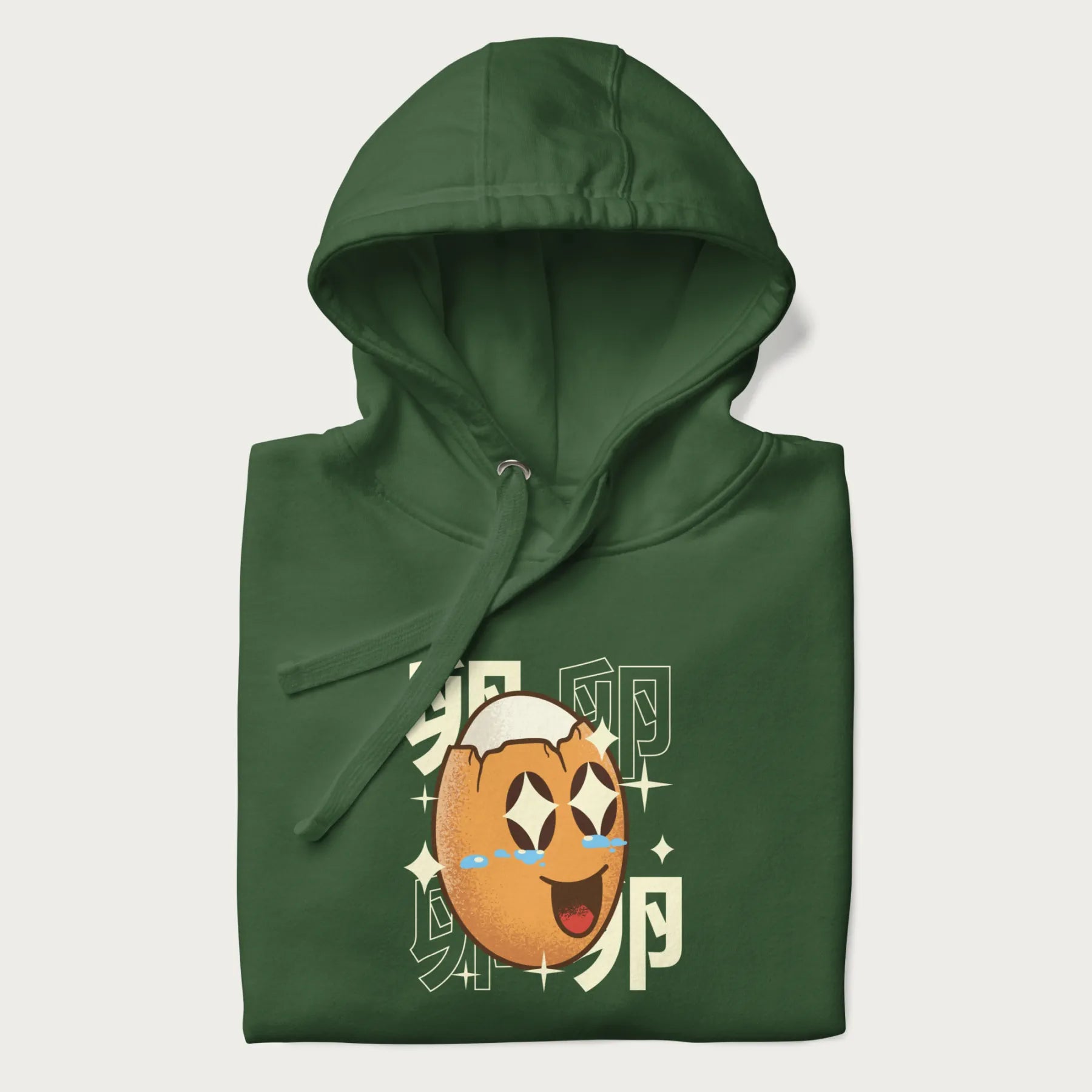 Folded forest green hoodie with Japanese graphic of a smiling egg with tears of joy, surrounded by the Japanese text '卵' (Egg).