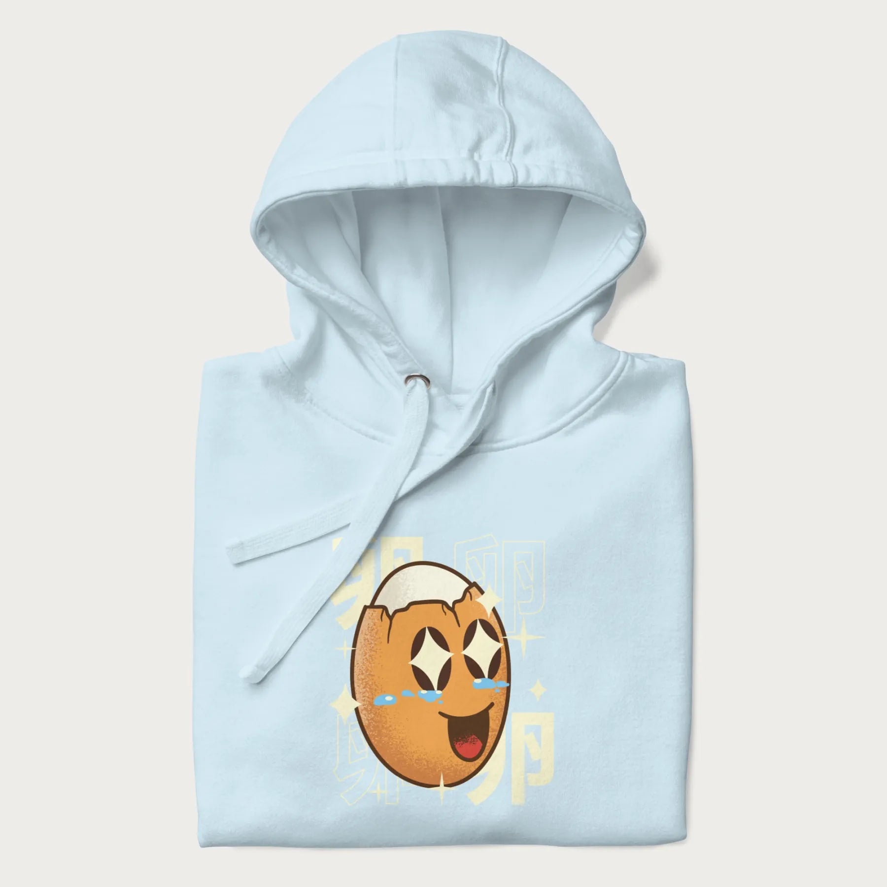 Folded light blue hoodie with Japanese graphic of a smiling egg with tears of joy, surrounded by the Japanese text '卵' (Egg).