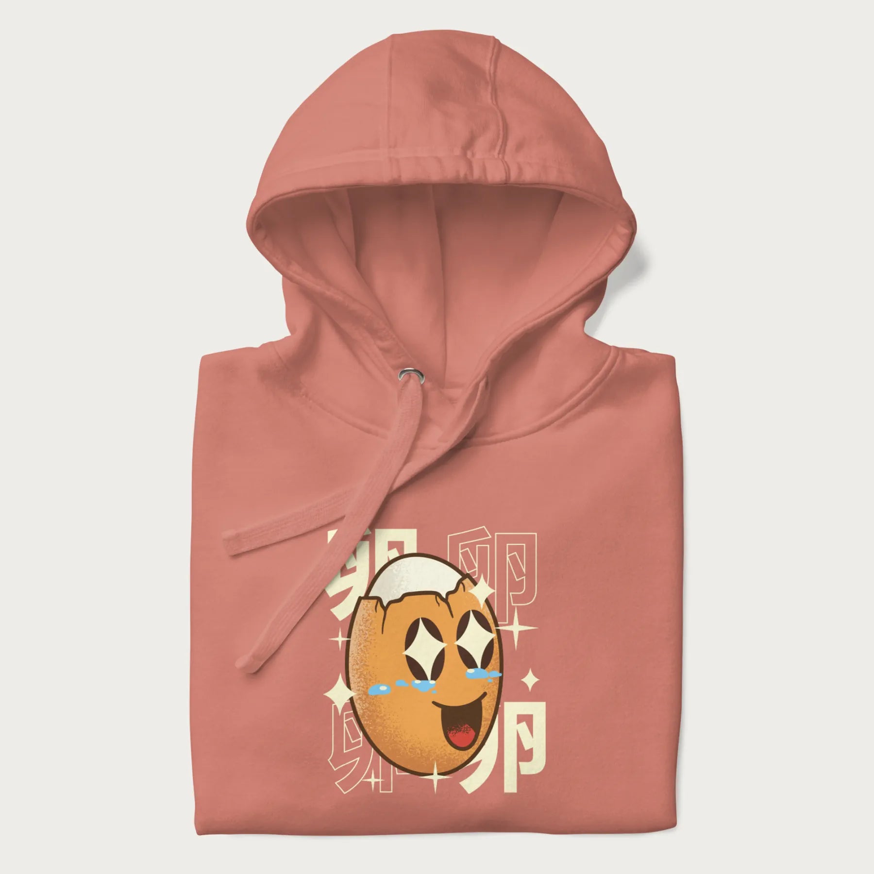 Folded light pink hoodie with Japanese graphic of a smiling egg with tears of joy, surrounded by the Japanese text '卵' (Egg).