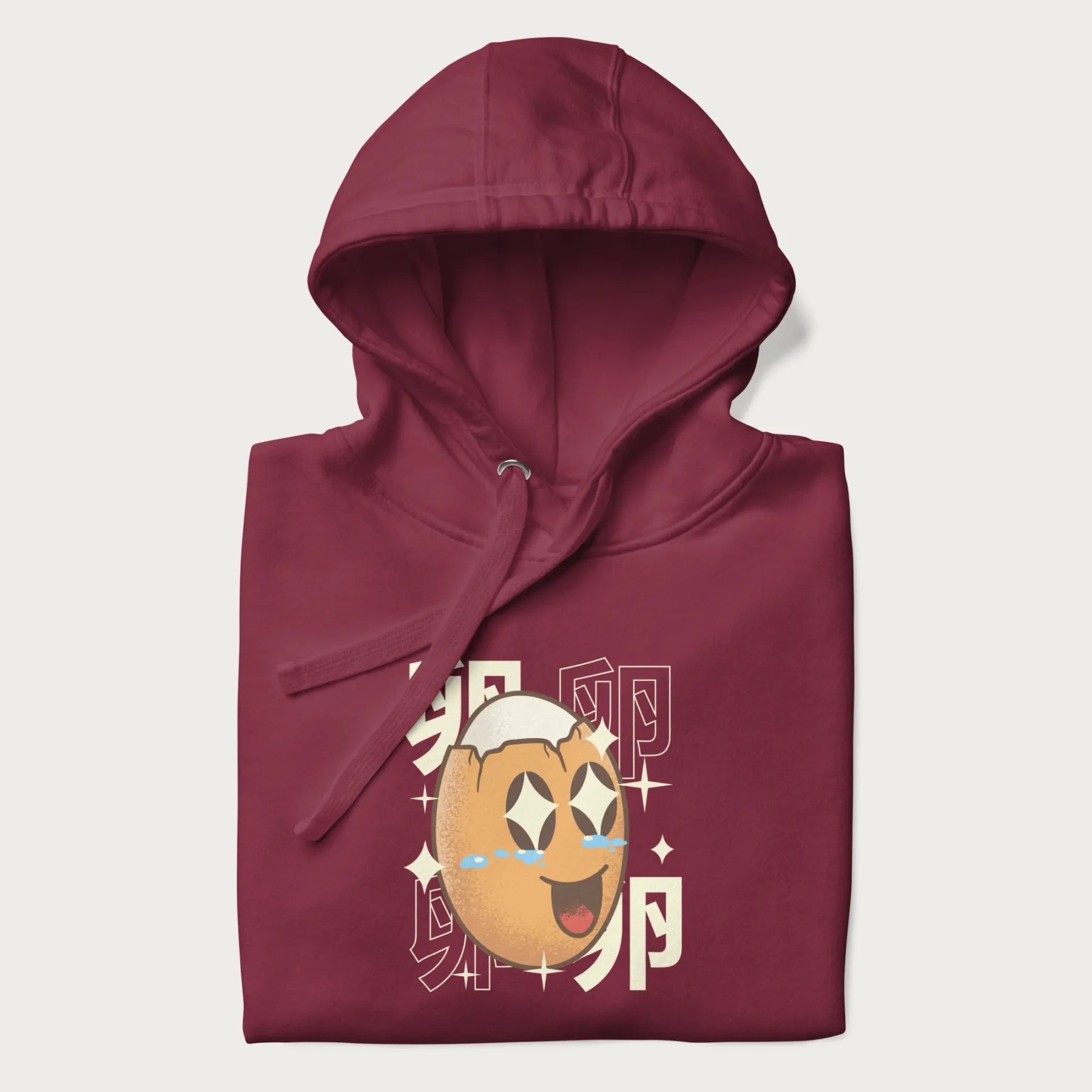 Folded maroon hoodie with Japanese graphic of a smiling egg with tears of joy, surrounded by the Japanese text '卵' (Egg).