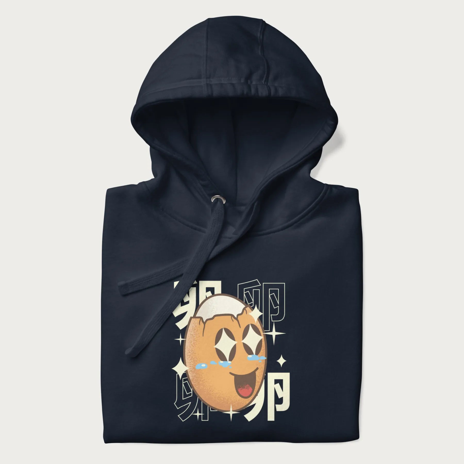 Folded navy blue hoodie with Japanese graphic of a smiling egg with tears of joy, surrounded by the Japanese text '卵' (Egg).