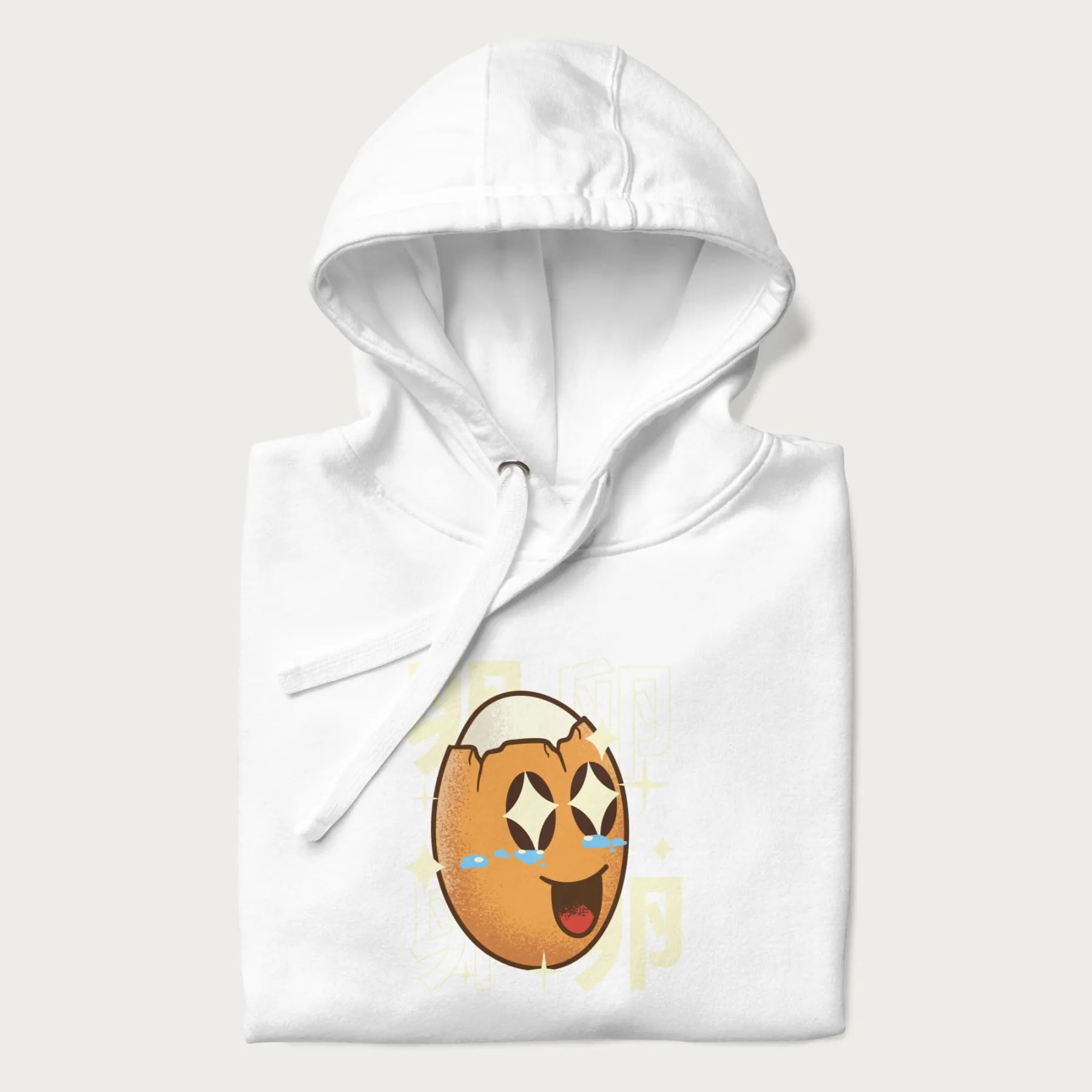 Folded white hoodie with Japanese graphic of a smiling egg with tears of joy, surrounded by the Japanese text '卵' (Egg).