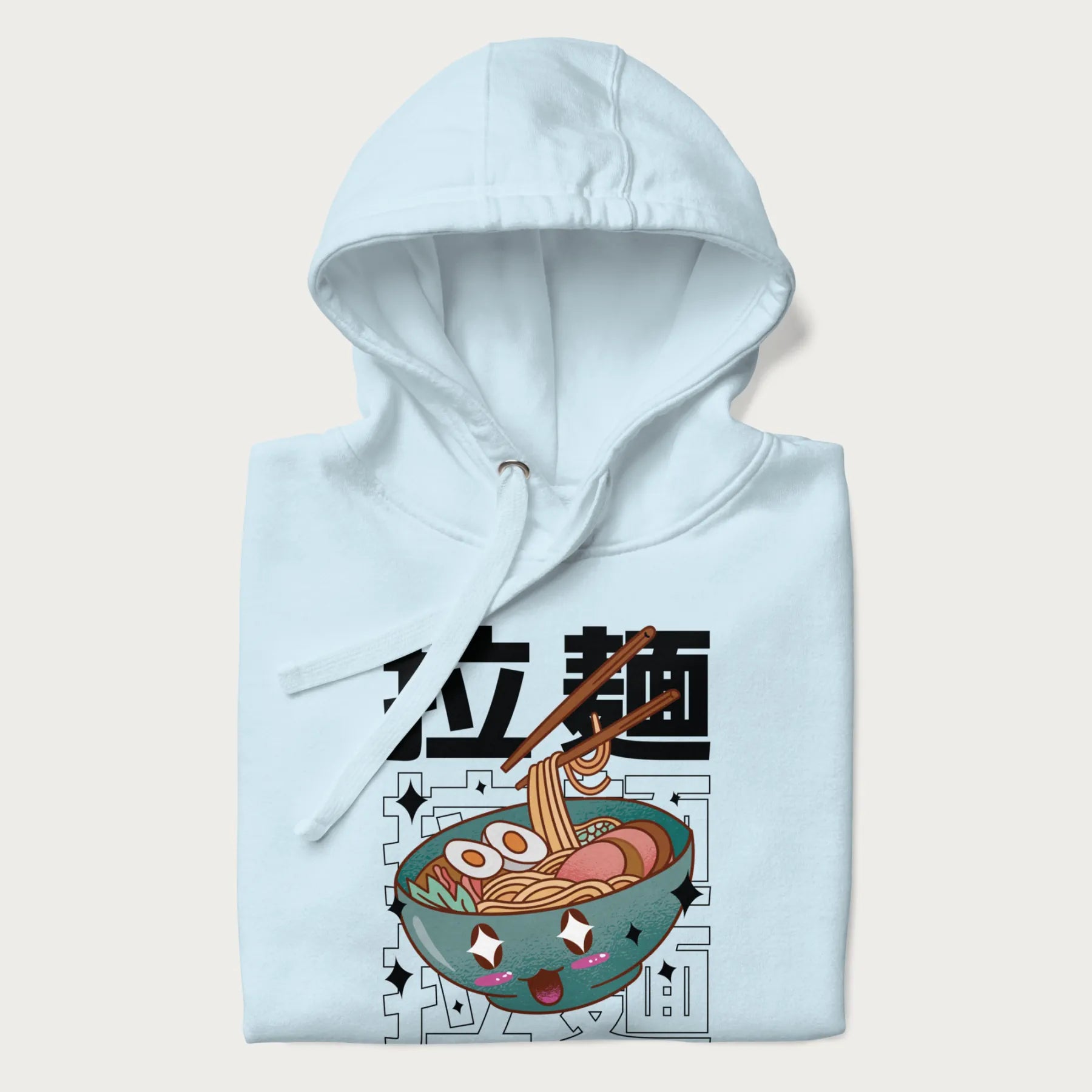 Folded light blue hoodie with Japanese text '拉麵' (Ramen) and graphic of a kawaii ramen bowl with sparkling eyes and blushed cheeks.