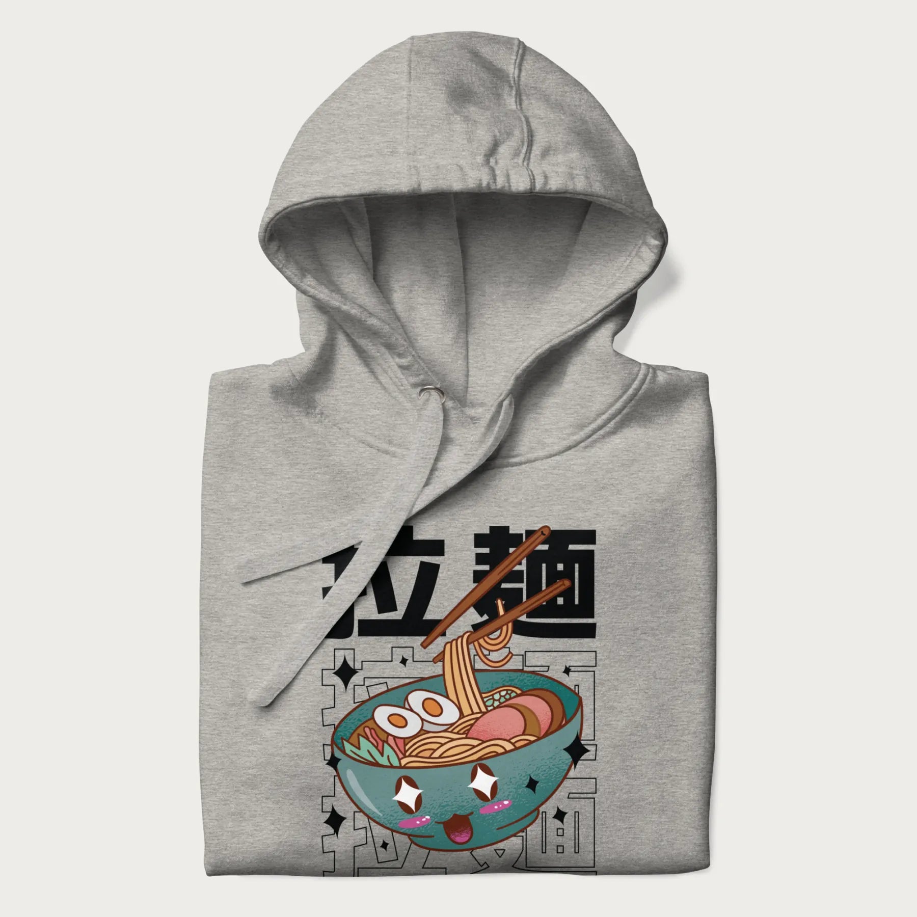 Folded light grey hoodie with Japanese text '拉麵' (Ramen) and graphic of a kawaii ramen bowl with sparkling eyes and blushed cheeks.
