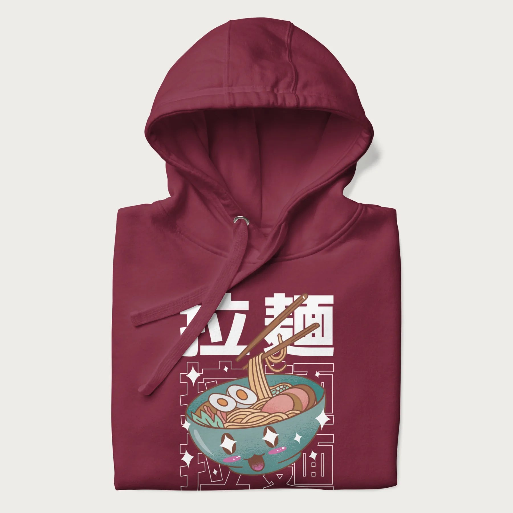 Folded maroon hoodie with Japanese text '拉麵' (Ramen) and graphic of a kawaii ramen bowl with sparkling eyes and blushed cheeks.