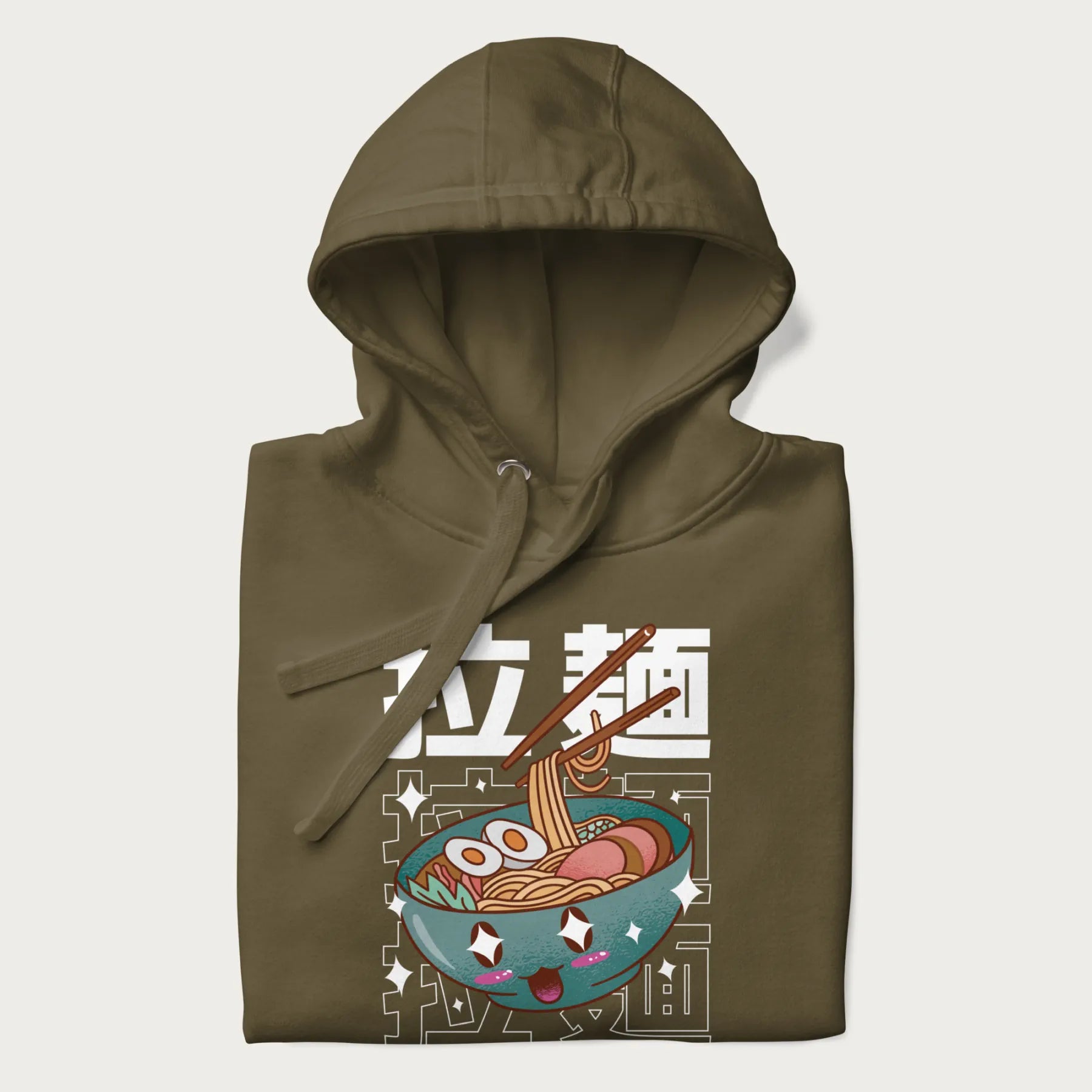 Folded military green hoodie with Japanese text '拉麵' (Ramen) and graphic of a kawaii ramen bowl with sparkling eyes and blushed cheeks.