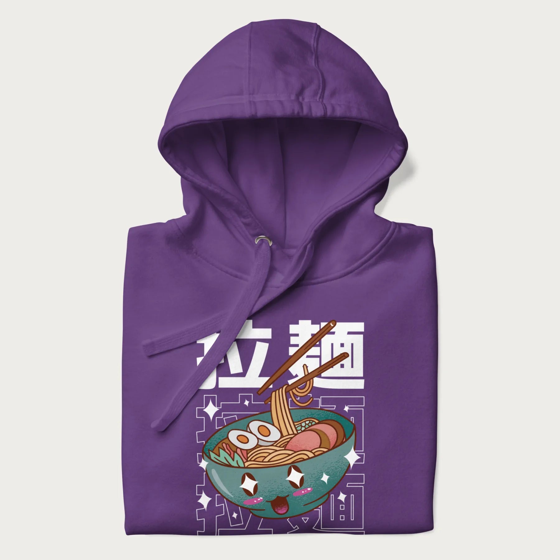 Folded purple hoodie with Japanese text '拉麵' (Ramen) and graphic of a kawaii ramen bowl with sparkling eyes and blushed cheeks.