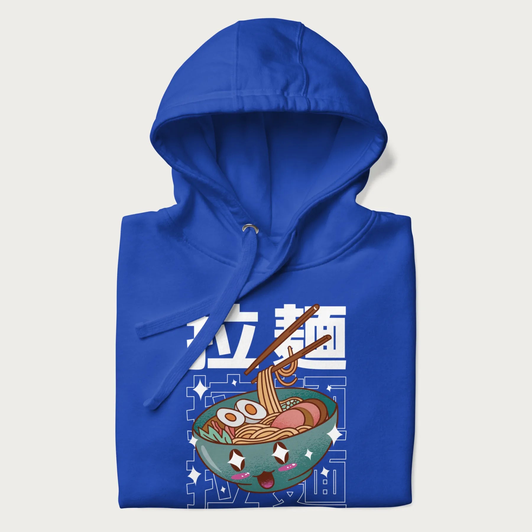 Folded royal blue hoodie with Japanese text '拉麵' (Ramen) and graphic of a kawaii ramen bowl with sparkling eyes and blushed cheeks.
