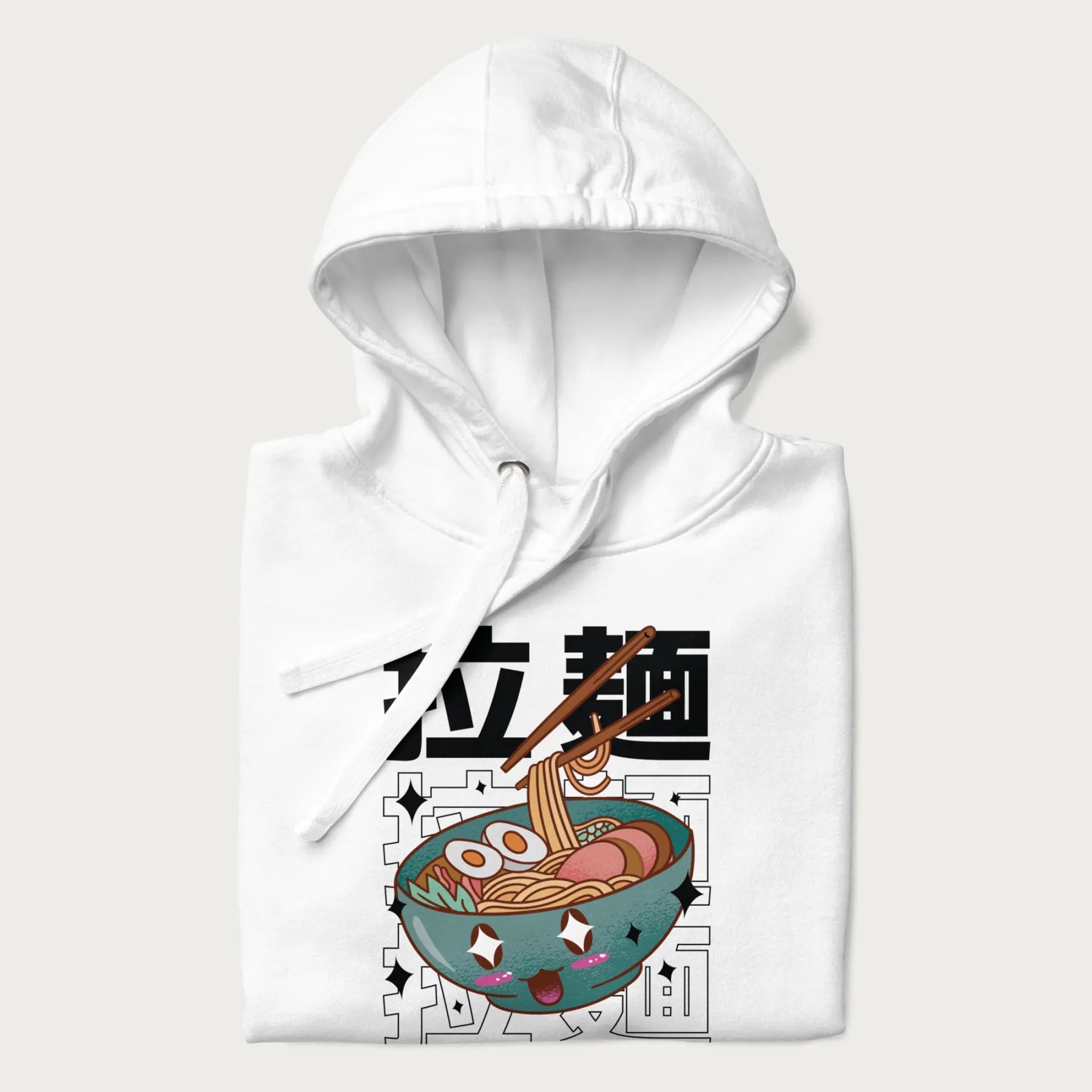Folded white hoodie with Japanese text '拉麵' (Ramen) and graphic of a kawaii ramen bowl with sparkling eyes and blushed cheeks.