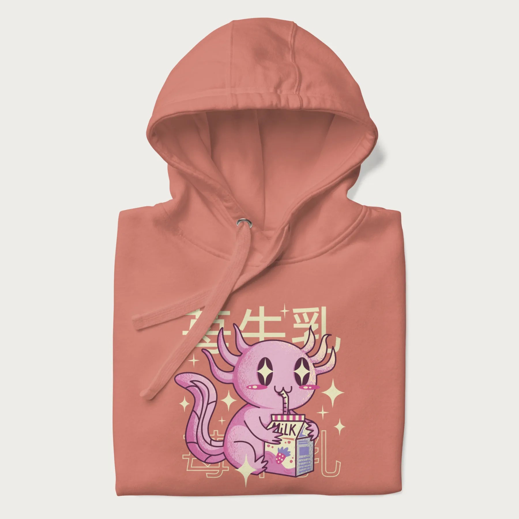 Folded light pink hoodie with Japanese graphic of a cute pink axolotl sipping strawberry milk from a carton, with Japanese text '苺牛乳' (Strawberry Milk).