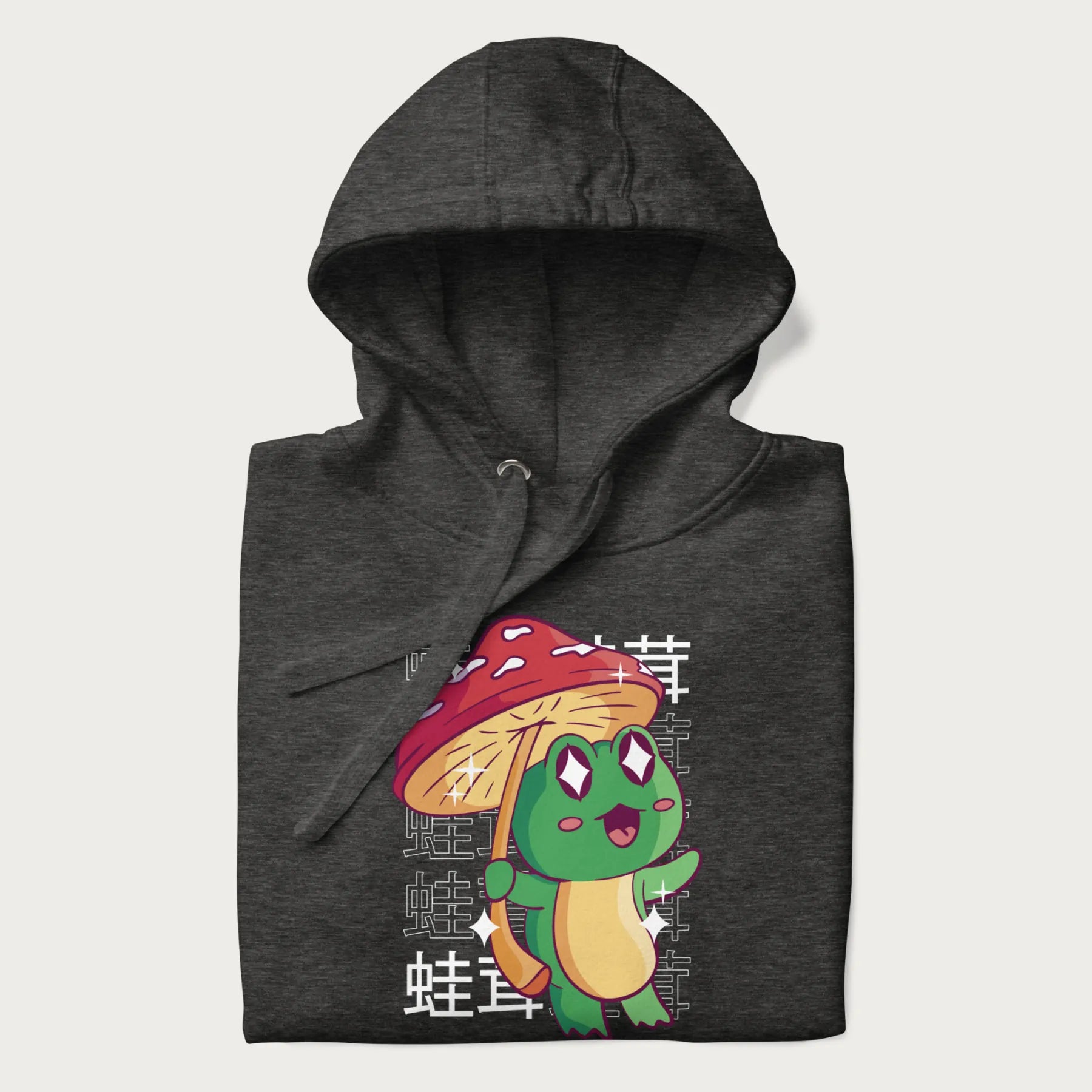 Folded dark grey hoodie with Japanese graphic of a cute green frog holding a red mushroom and Japanese text '蛙茸' in the background.