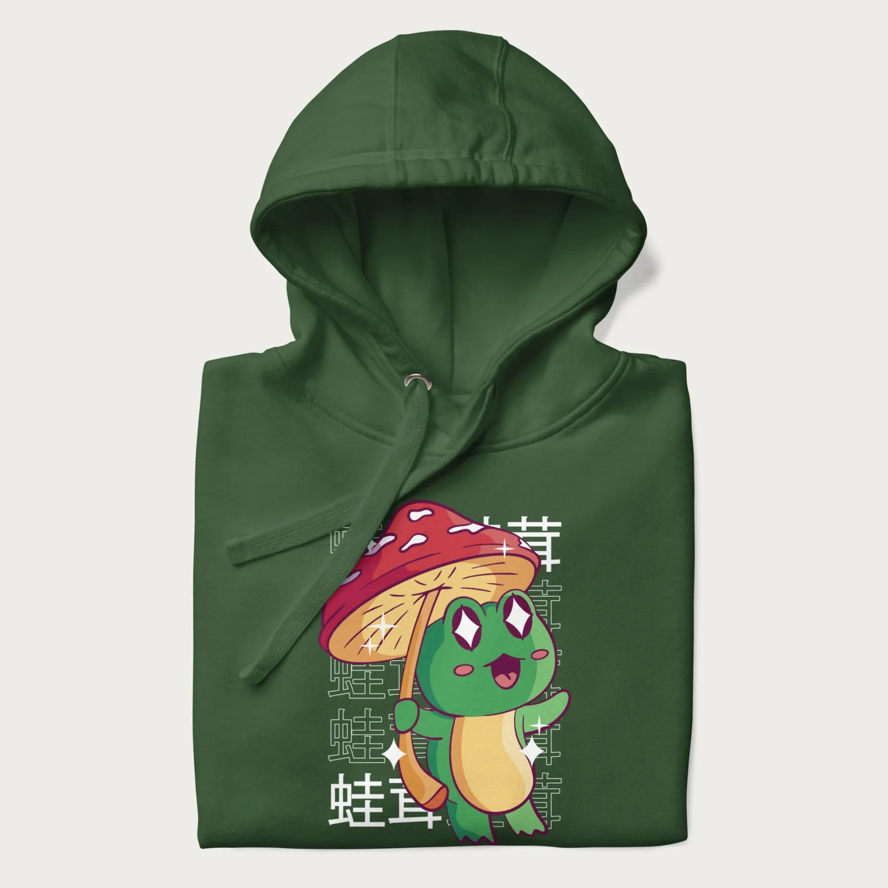 Folded forest green hoodie with Japanese graphic of a cute green frog holding a red mushroom and Japanese text '蛙茸' in the background.