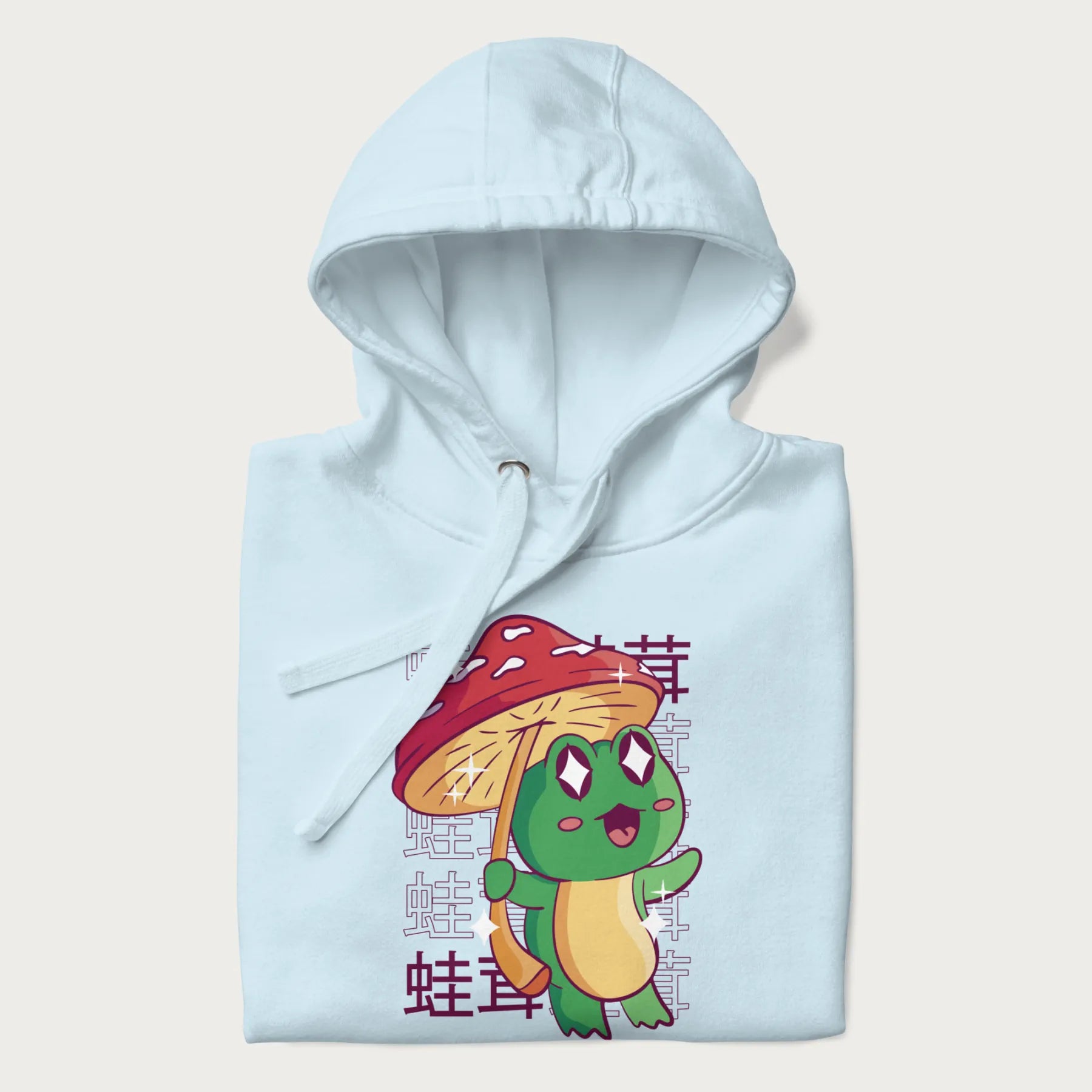 Folded light blue hoodie with Japanese graphic of a cute green frog holding a red mushroom and Japanese text '蛙茸' in the background.