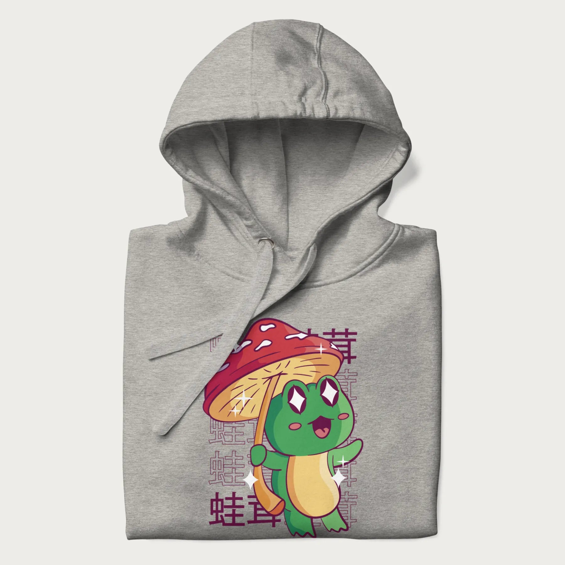 Folded light grey hoodie with Japanese graphic of a cute green frog holding a red mushroom and Japanese text '蛙茸' in the background.