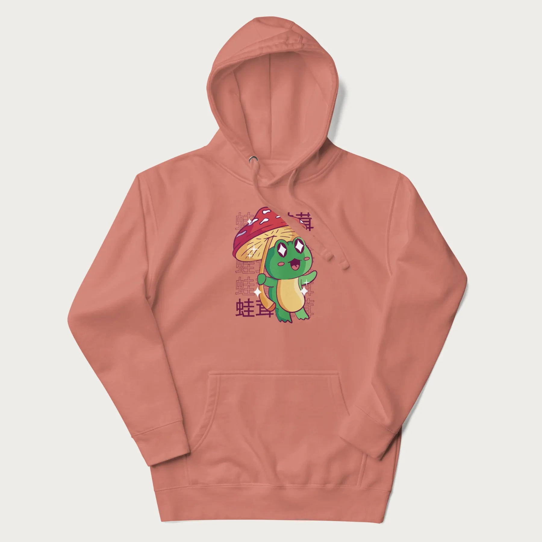Light pink hoodie with Japanese graphic of a cute green frog holding a red mushroom and Japanese text '蛙茸' in the background.