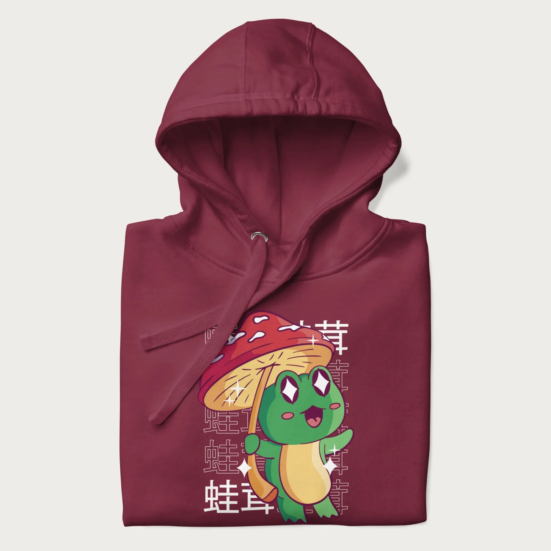 Folded maroon hoodie with Japanese graphic of a cute green frog holding a red mushroom and Japanese text '蛙茸' in the background.