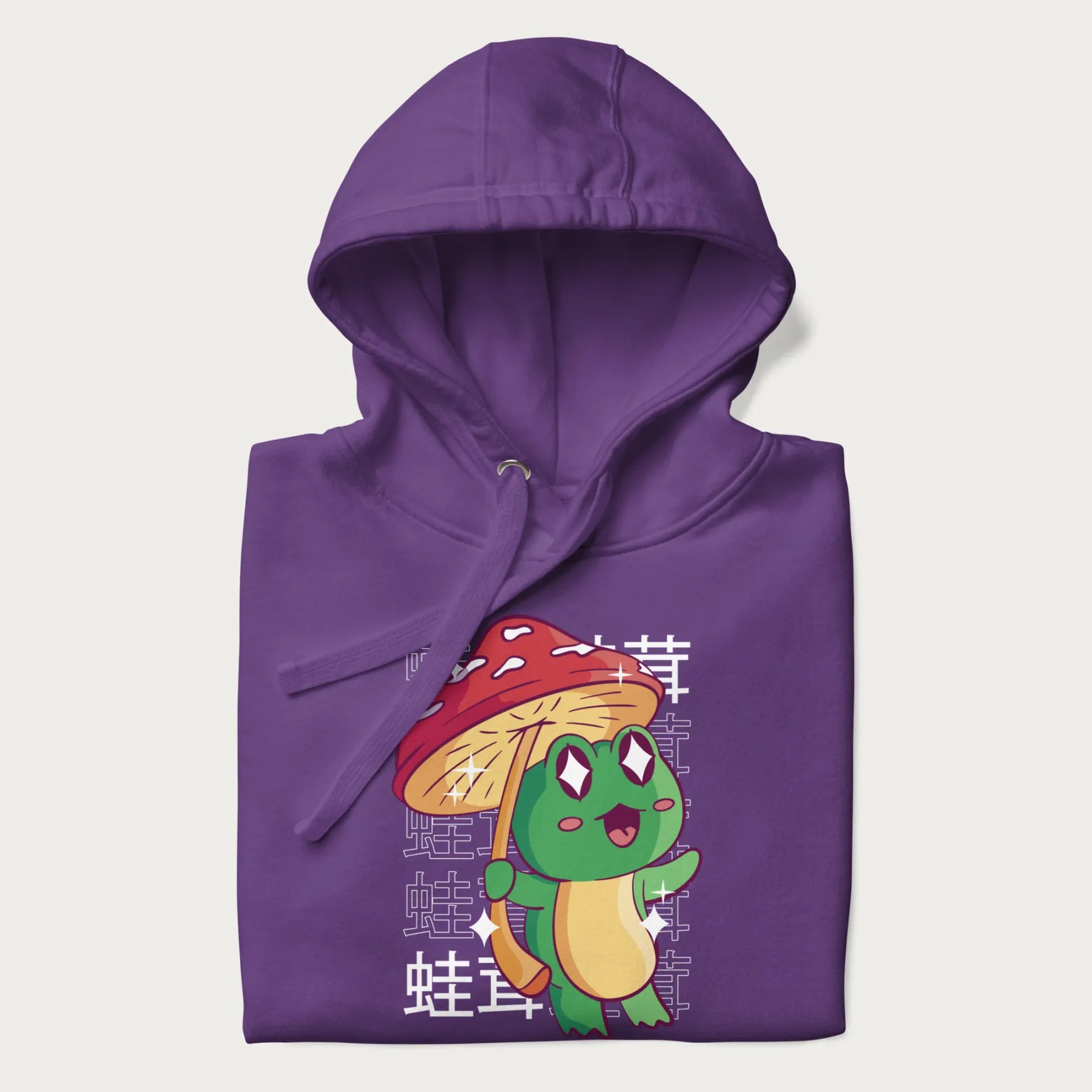 Folded purple hoodie with Japanese graphic of a cute green frog holding a red mushroom and Japanese text '蛙茸' in the background.