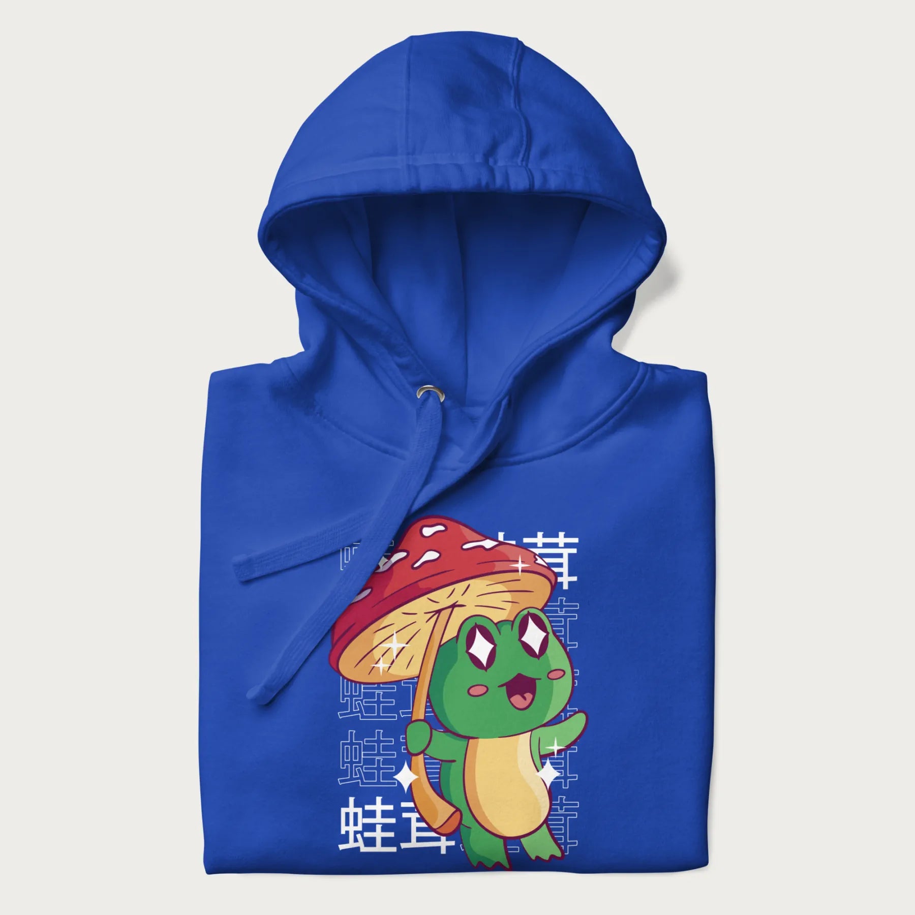 Folded royal blue hoodie with Japanese graphic of a cute green frog holding a red mushroom and Japanese text '蛙茸' in the background.