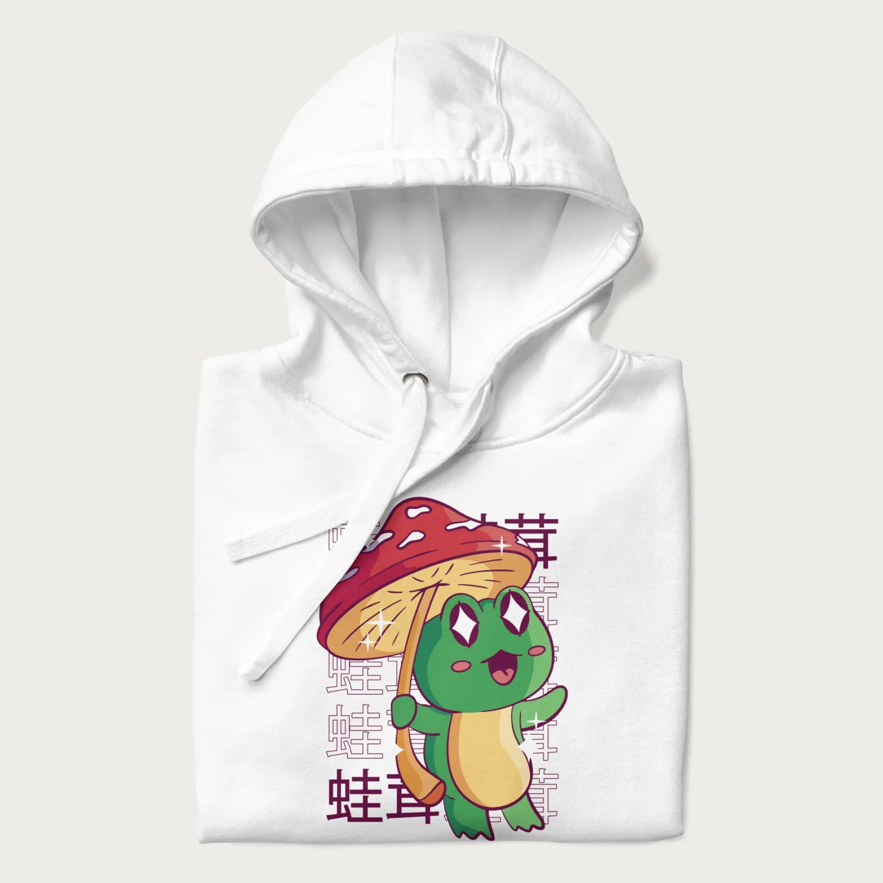 Folded white hoodie with Japanese graphic of a cute green frog holding a red mushroom and Japanese text '蛙茸' in the background.