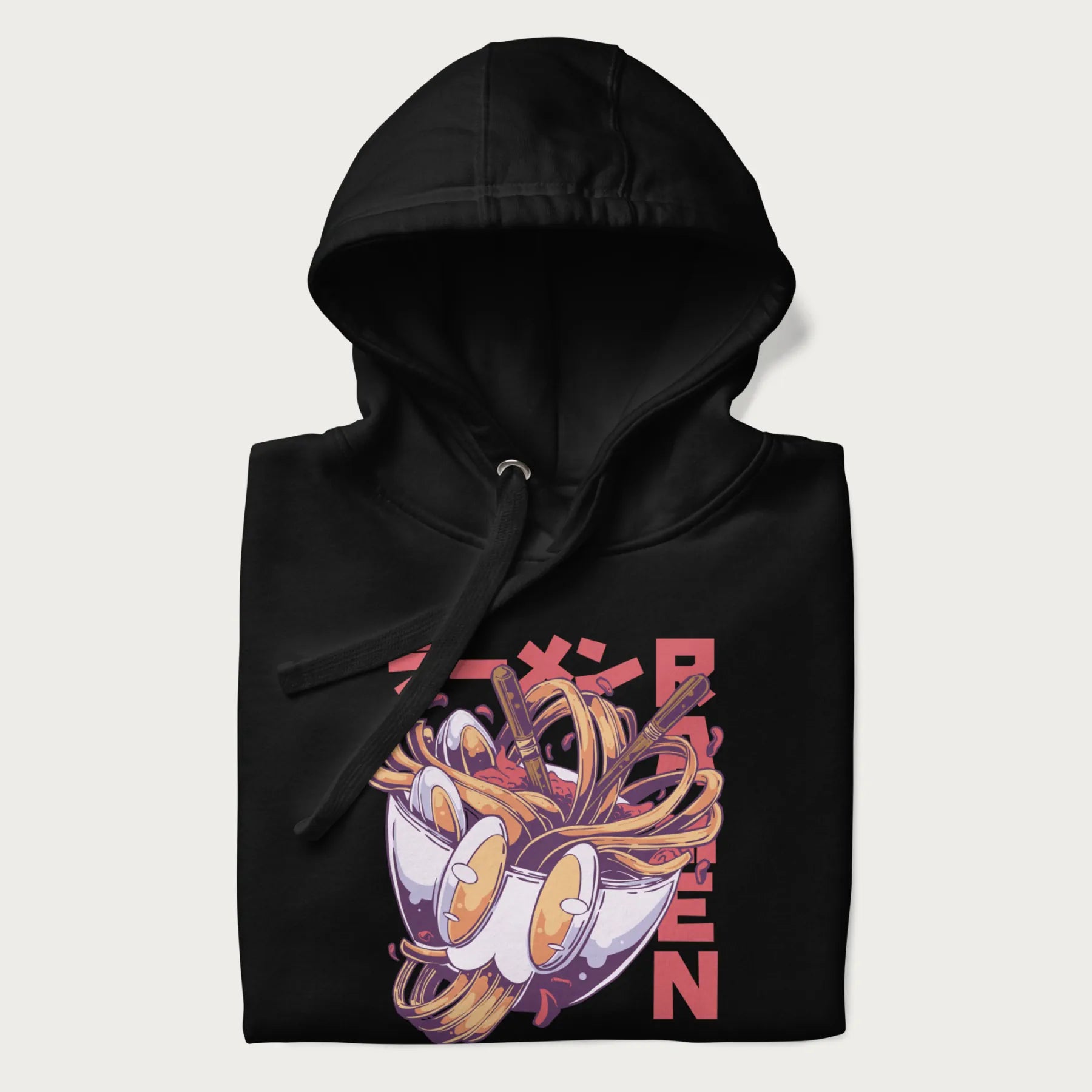 Folded black hoodie with Japanese graphic of a ramen bowl with noodles, eggs and Japanese text 'ラーメン' (Ramen) in bold red text.