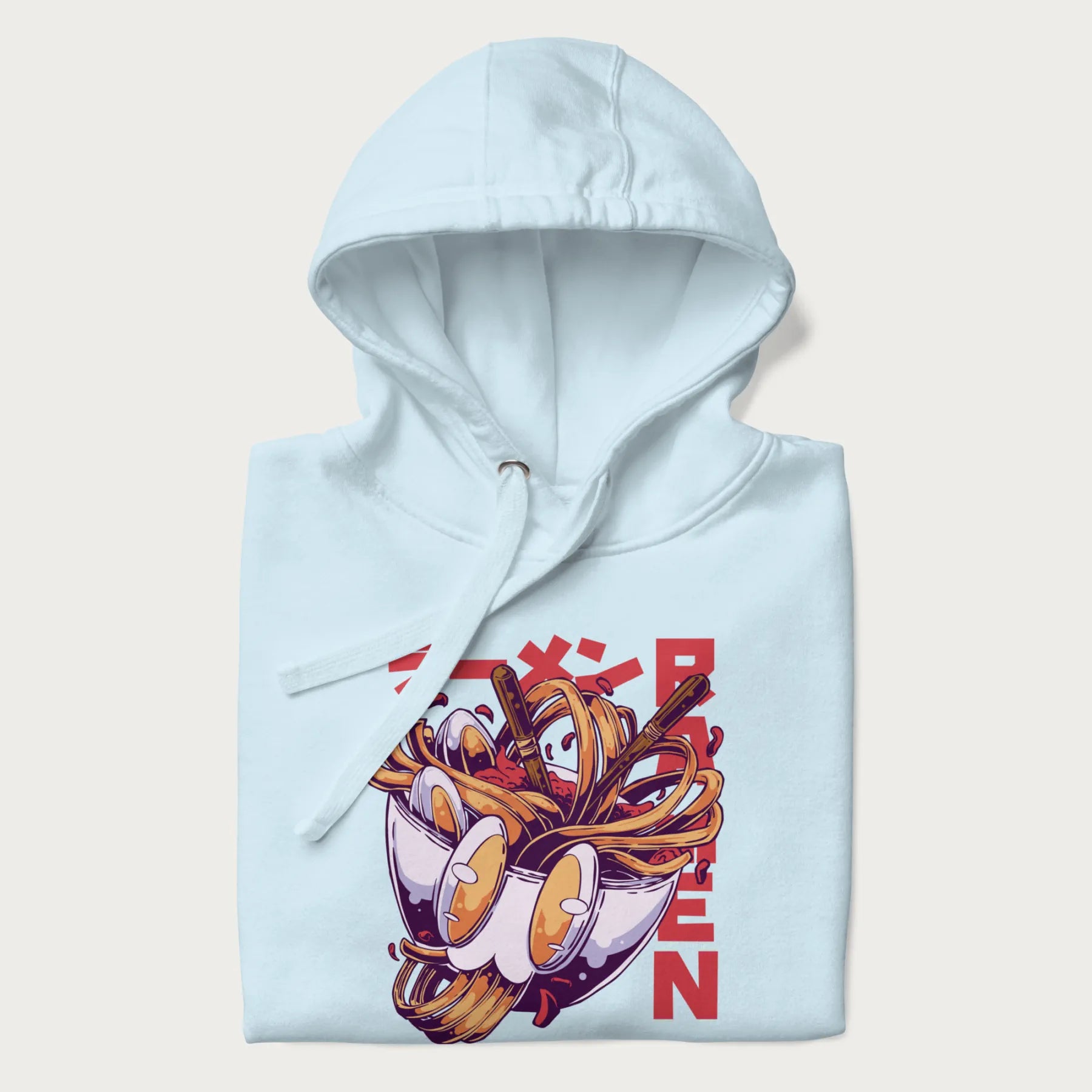 Folded light blue hoodie with Japanese graphic of a ramen bowl with noodles, eggs and Japanese text 'ラーメン' (Ramen) in bold red text.