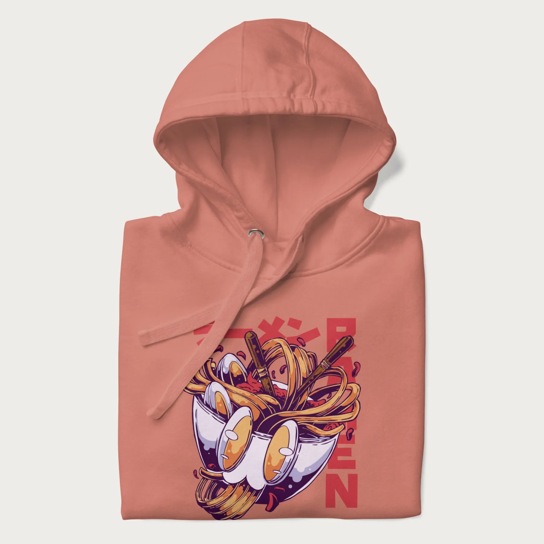 Folded light pink hoodie with Japanese graphic of a ramen bowl with noodles, eggs and Japanese text 'ラーメン' (Ramen) in bold red text.