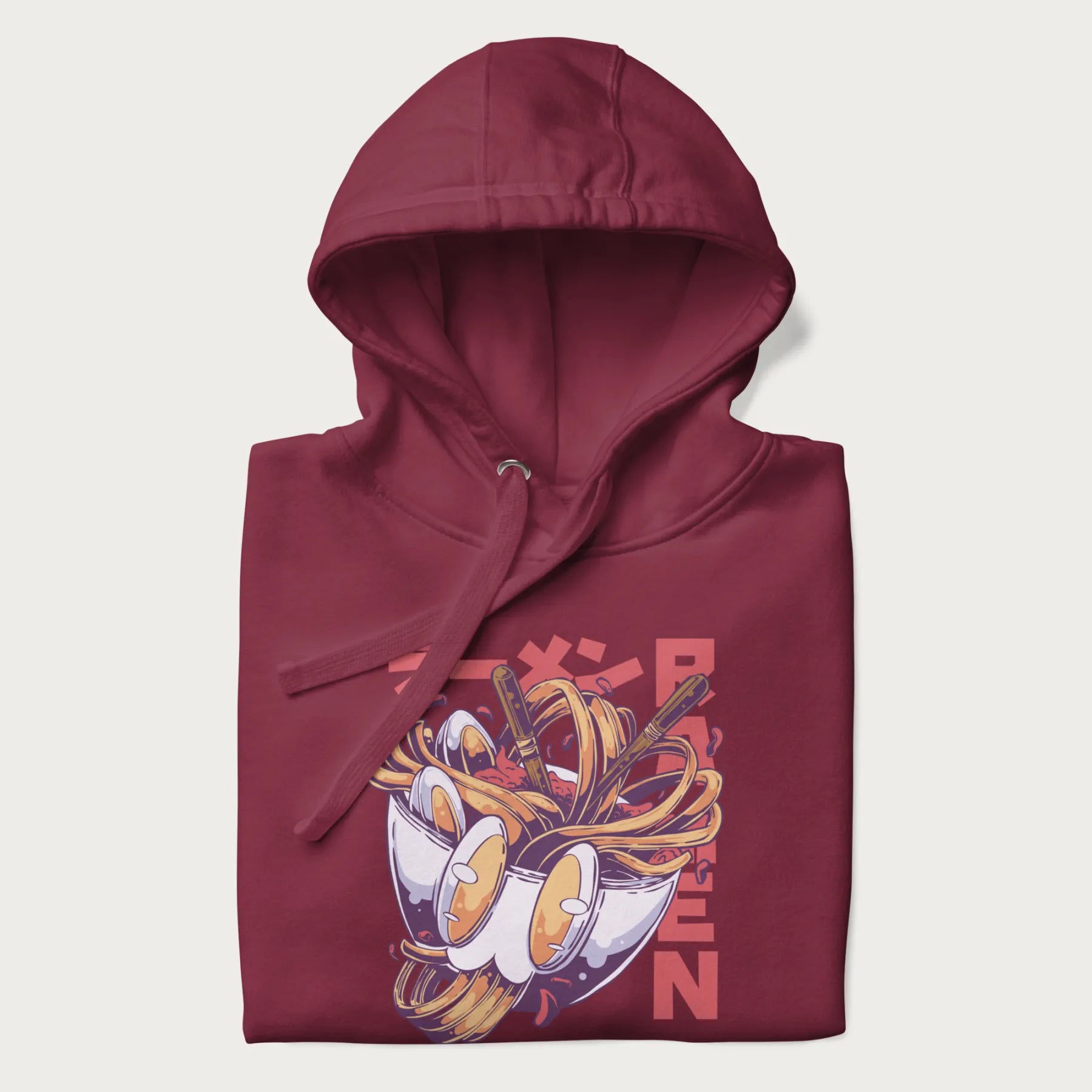 Folded maroon hoodie with Japanese graphic of a ramen bowl with noodles, eggs and Japanese text 'ラーメン' (Ramen) in bold red text.