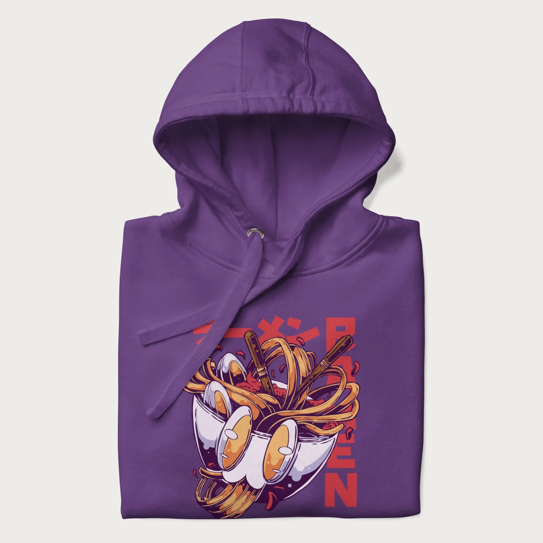 Folded purple hoodie with Japanese graphic of a ramen bowl with noodles, eggs and Japanese text 'ラーメン' (Ramen) in bold red text.