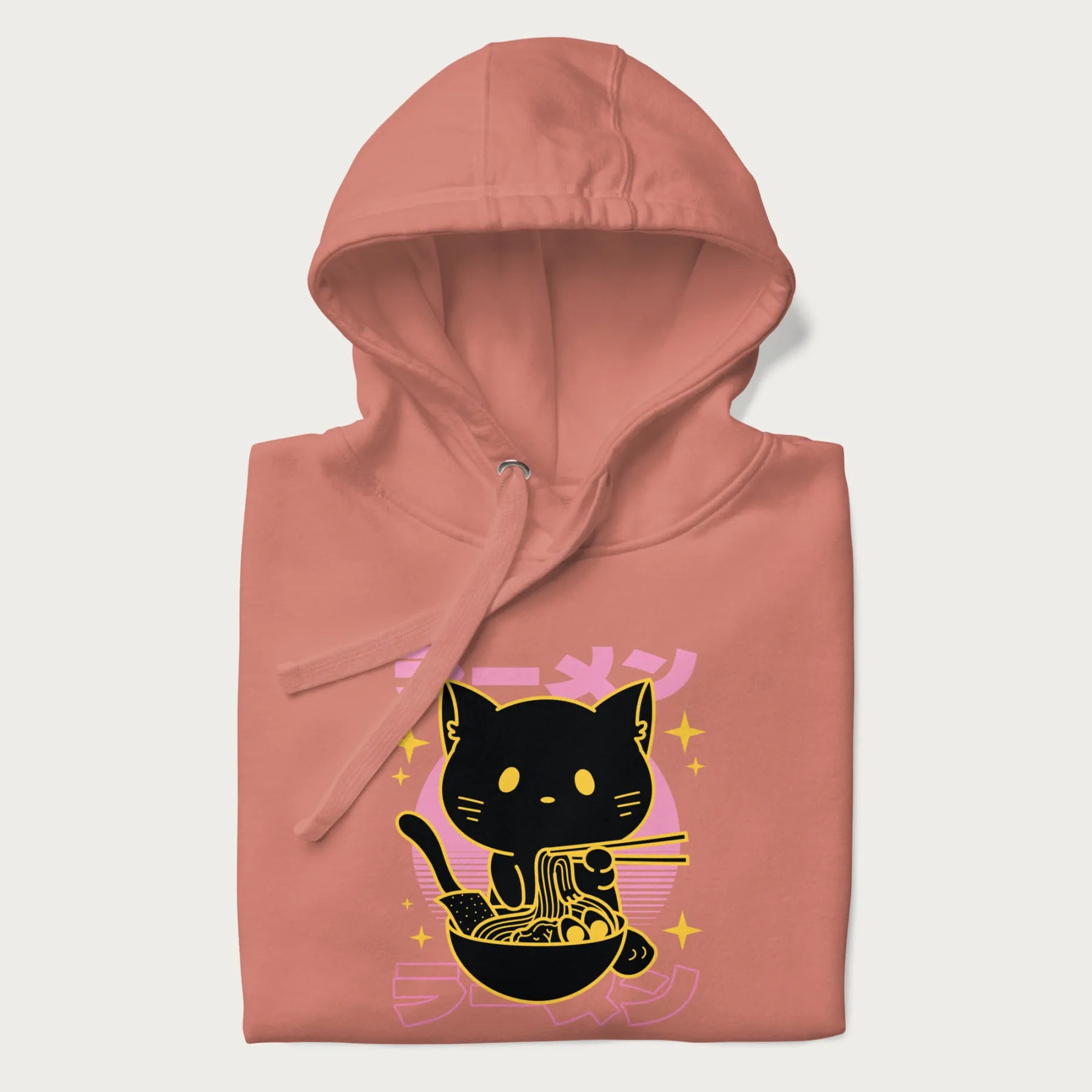 Folded light pink hoodie with Japanese text 'ラーメン' (ramen) and a retro design of a cute black cat eating ramen.