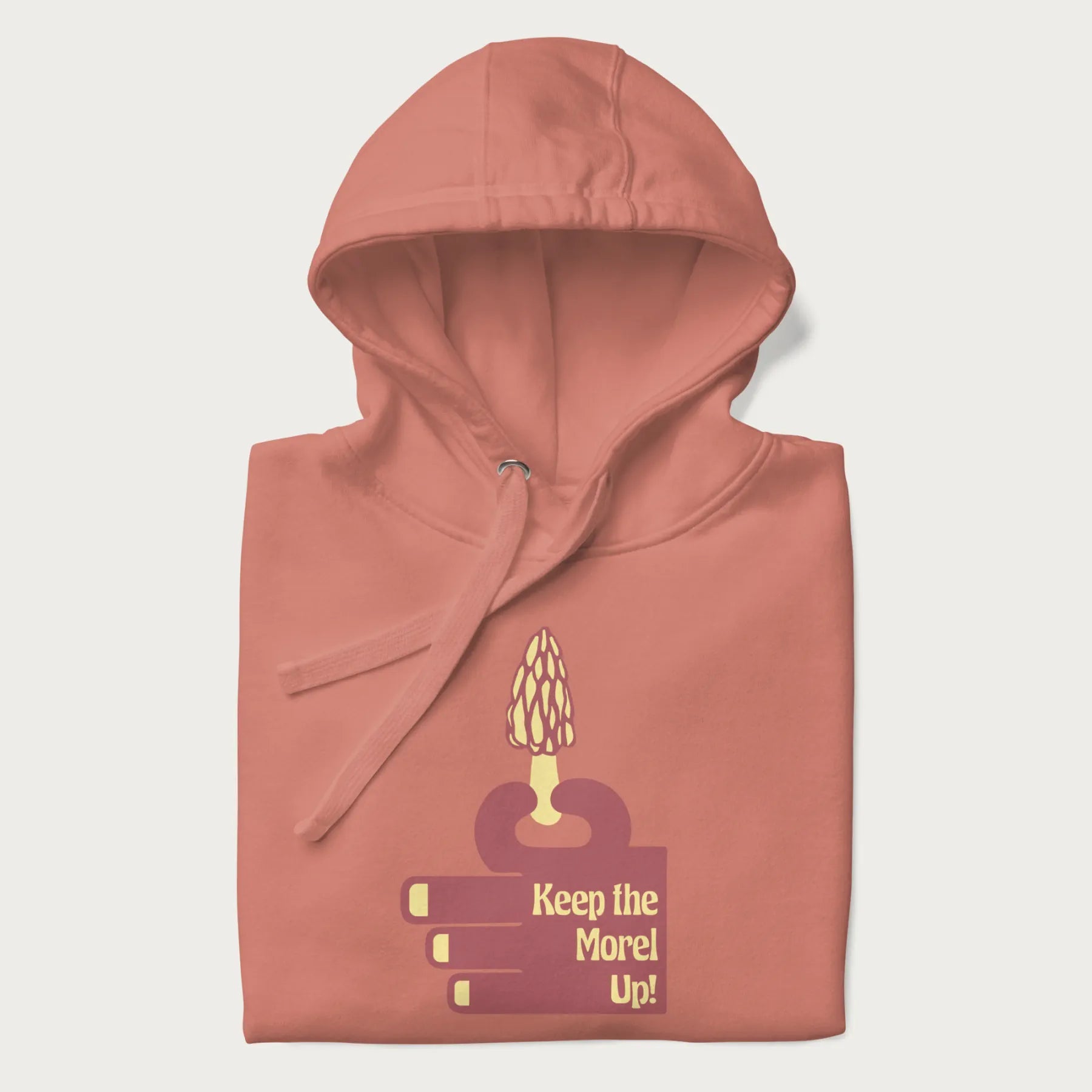 Folded light pink hoodie with a simple graphic of a hand holding a morel mushroom and the phrase 'Keep the Morel Up!'