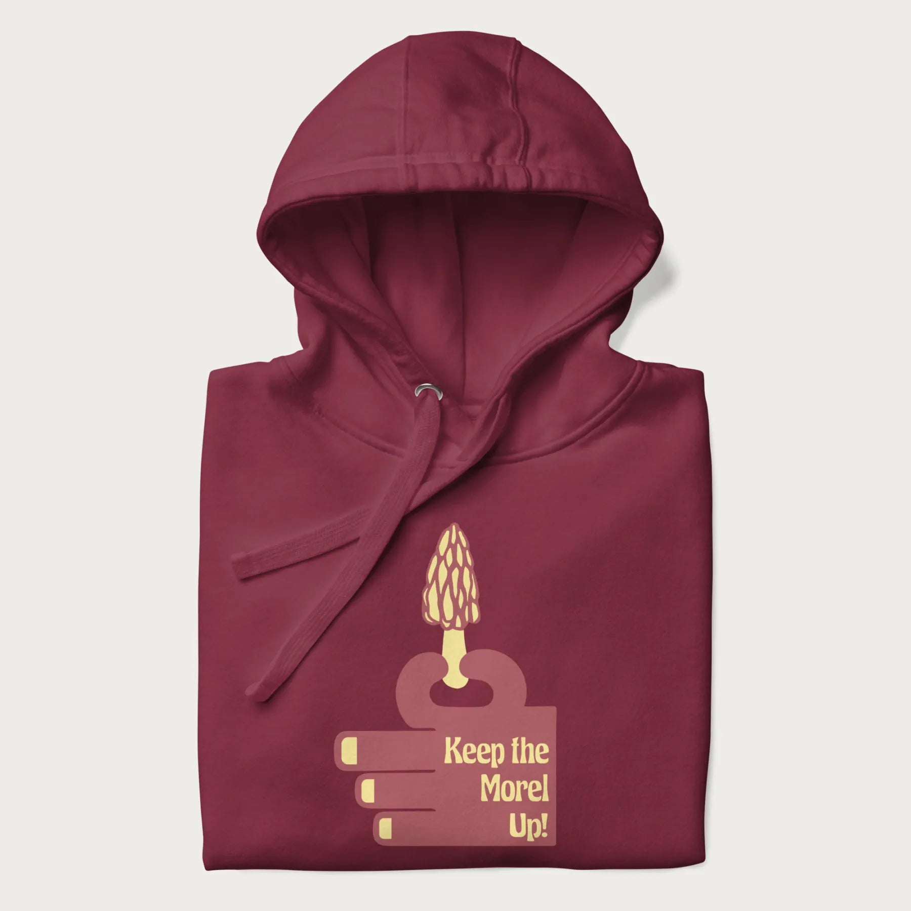 Folded maroon hoodie with a simple graphic of a hand holding a morel mushroom and the phrase 'Keep the Morel Up!'