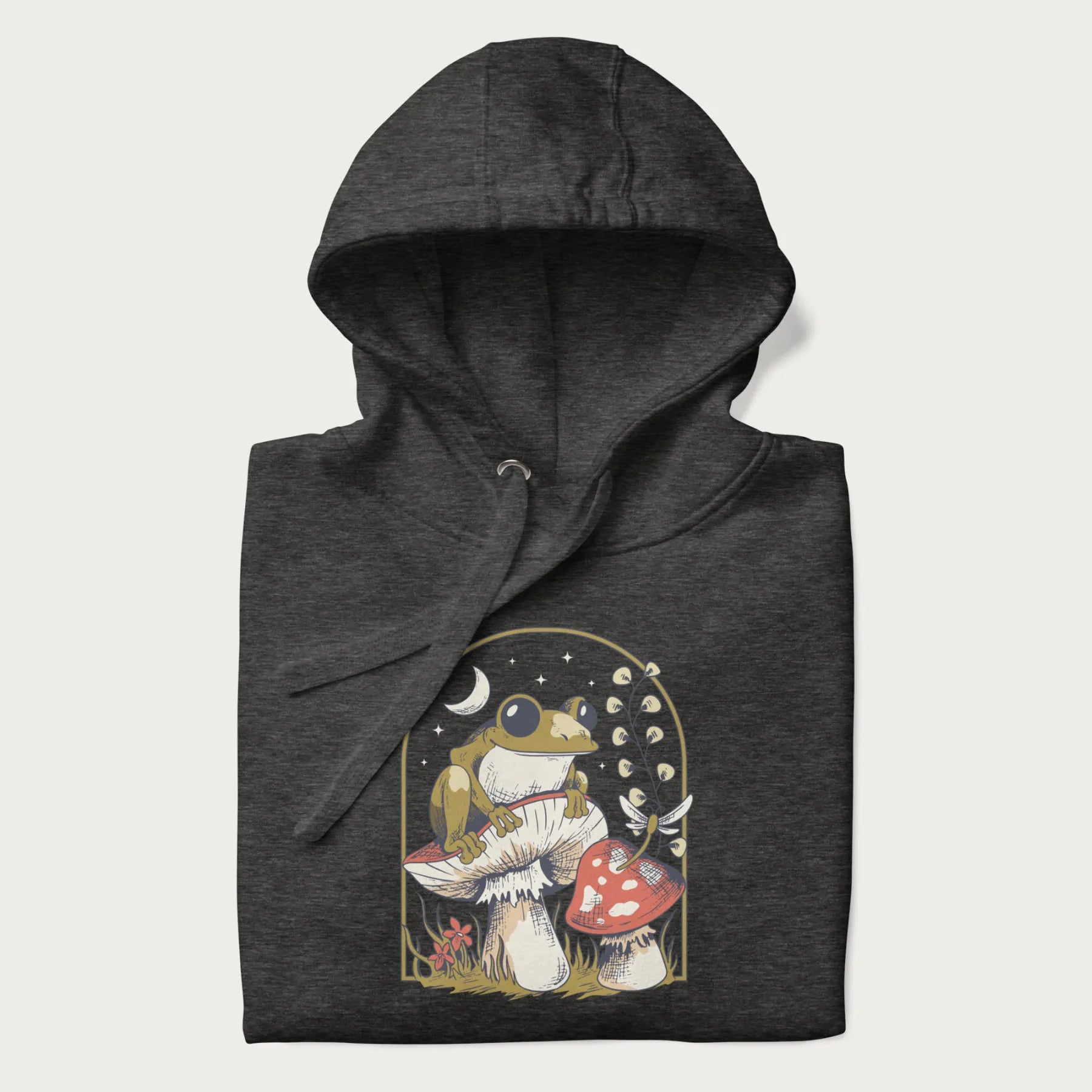 Folded dark grey hoodie with cottagecore graphic of a frog perched on a mushroom, surrounded by additional mushrooms, flowers, and a crescent moon with stars.