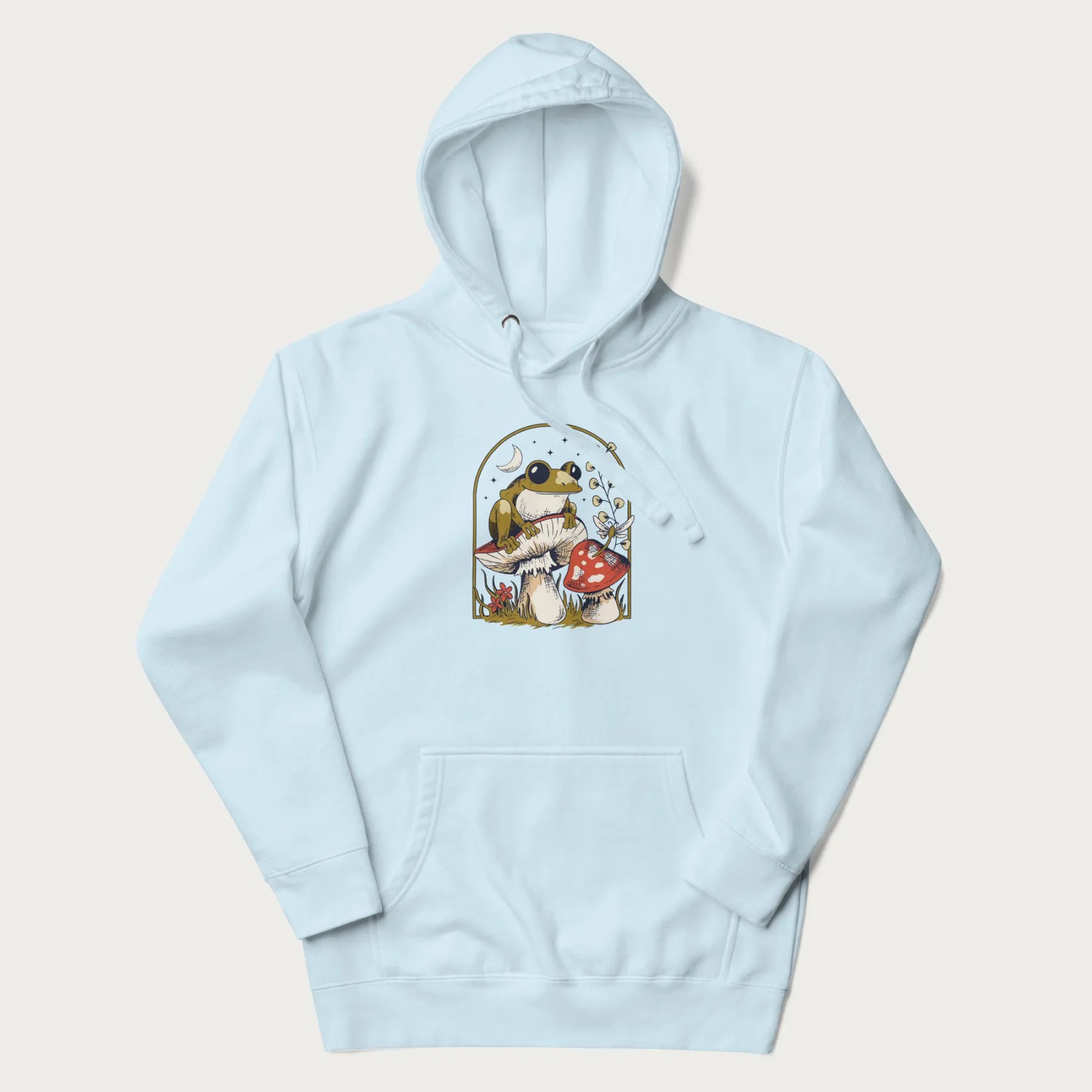 Light blue hoodie with cottagecore graphic of a frog perched on a mushroom, surrounded by additional mushrooms, flowers, and a crescent moon with stars.