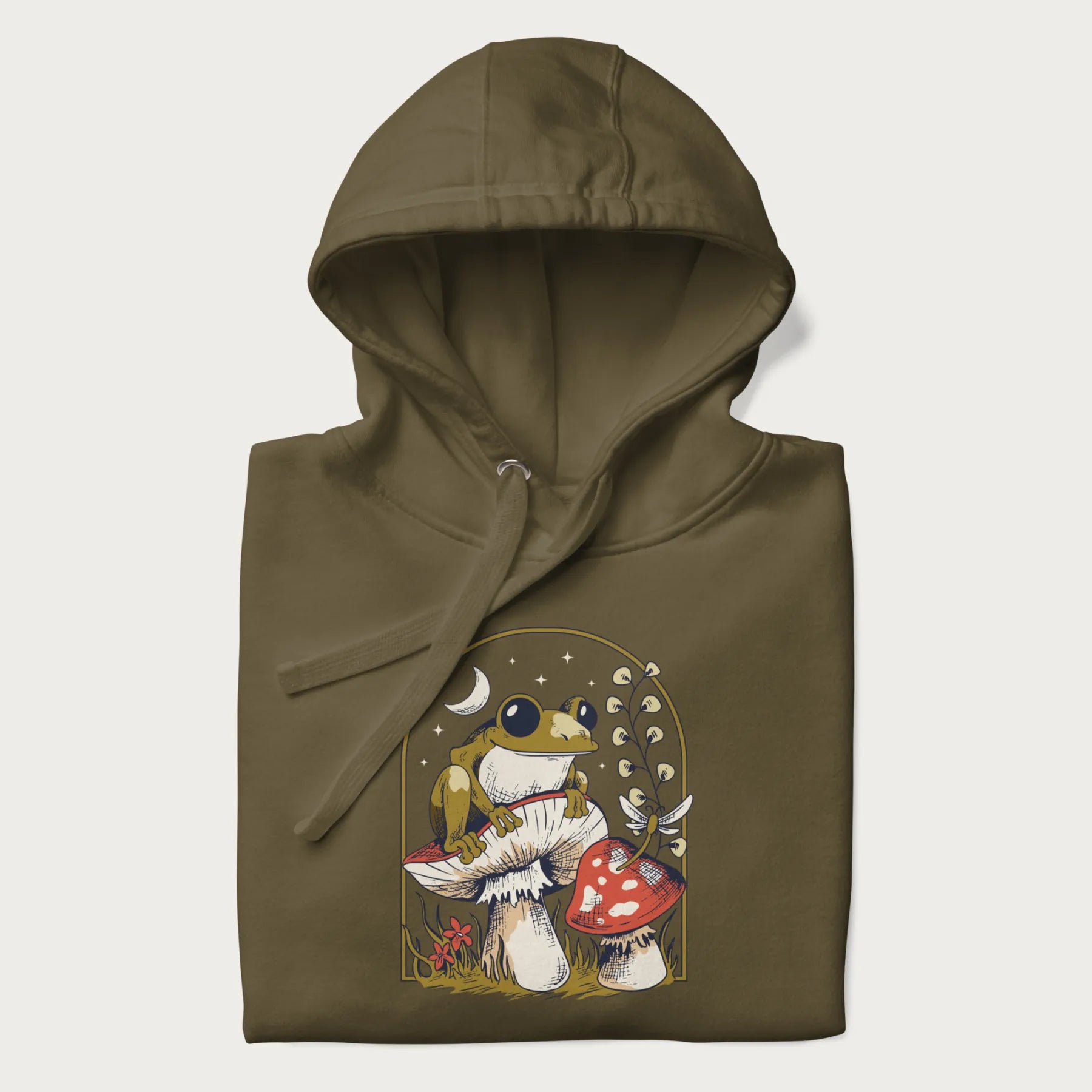 Folded military green hoodie with cottagecore graphic of a frog perched on a mushroom, surrounded by additional mushrooms, flowers, and a crescent moon with stars.