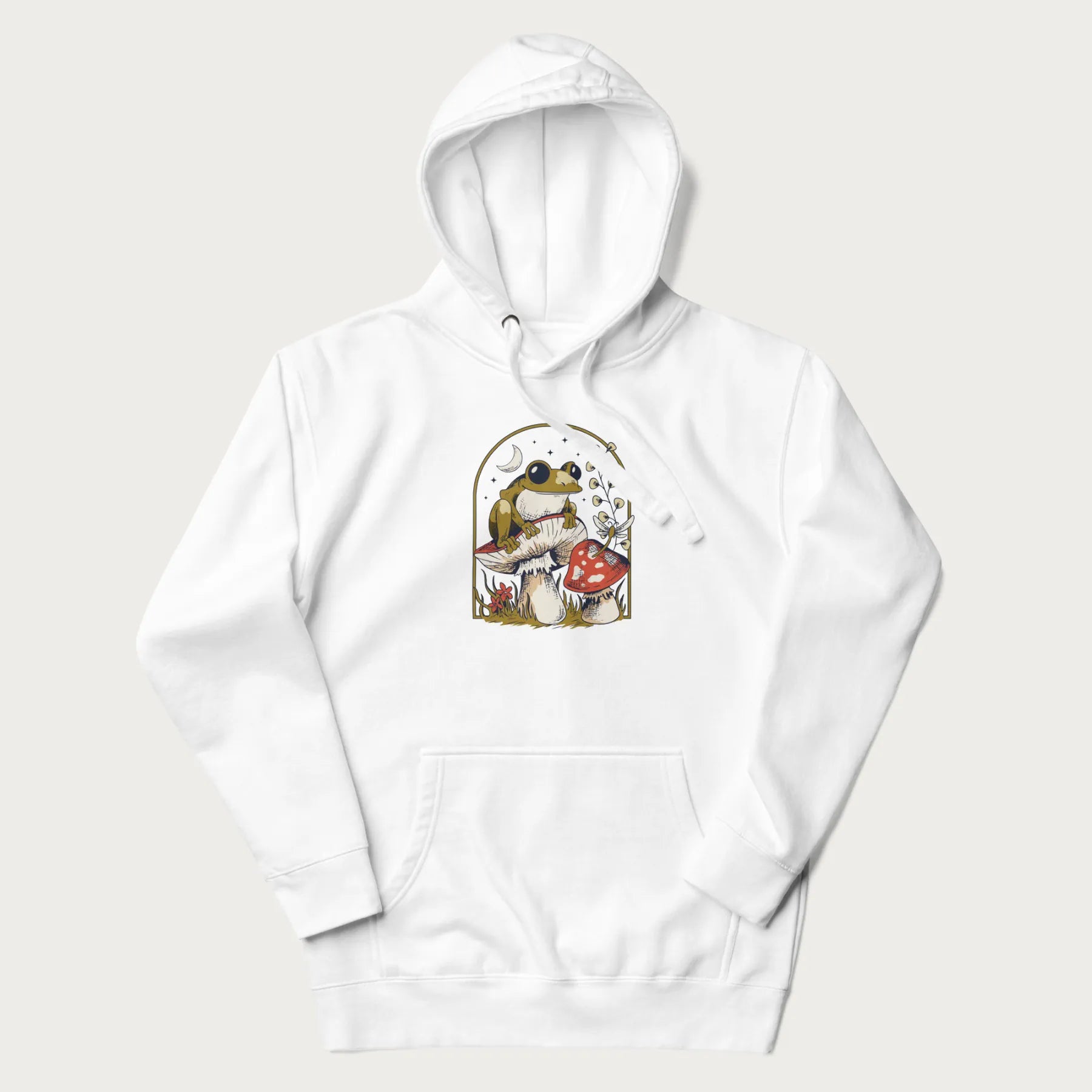 White hoodie with cottagecore graphic of a frog perched on a mushroom, surrounded by additional mushrooms, flowers, and a crescent moon with stars.