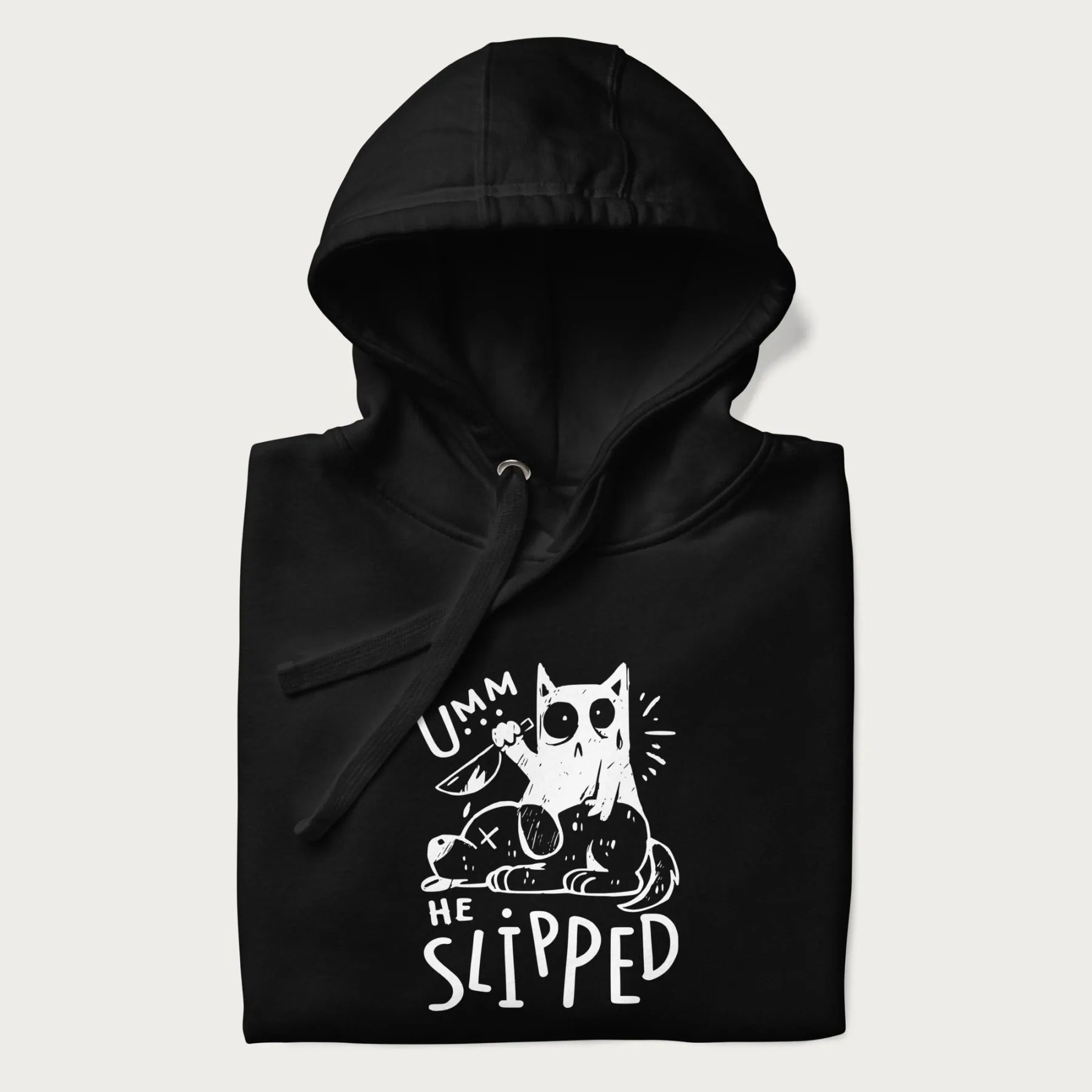 Folded black hoodie with a graphic of a white cat holding a knife over a dog with a funny phrase 'Umm, He Slipped'.