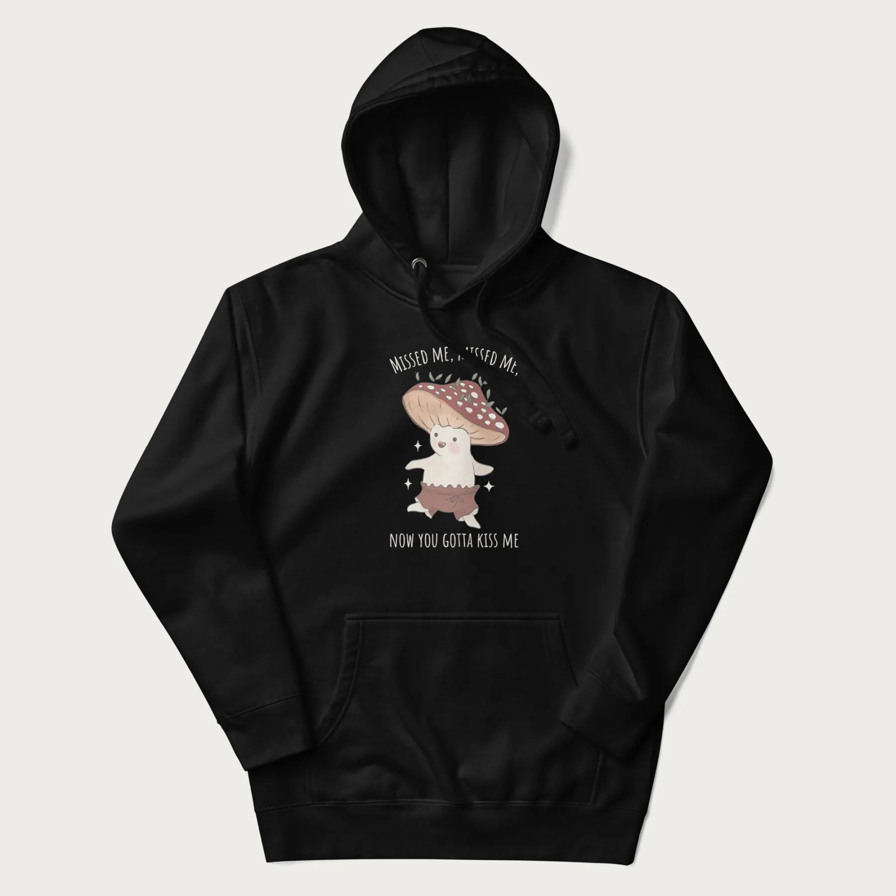 Black hoodie with a graphic of a cute cottagecore mushroom character dancing and the phrase 'Missed Me, Missed Me, Now You Gotta Kiss Me'.
