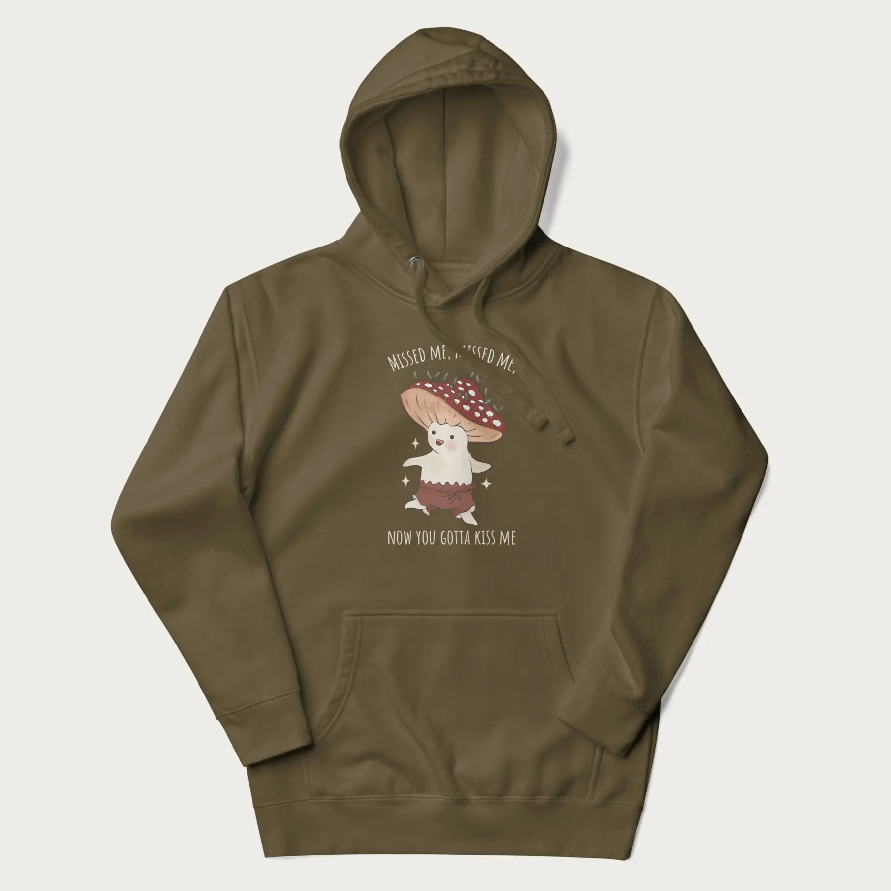 Military green hoodie with a graphic of a cute cottagecore mushroom character dancing and the phrase 'Missed Me, Missed Me, Now You Gotta Kiss Me'.