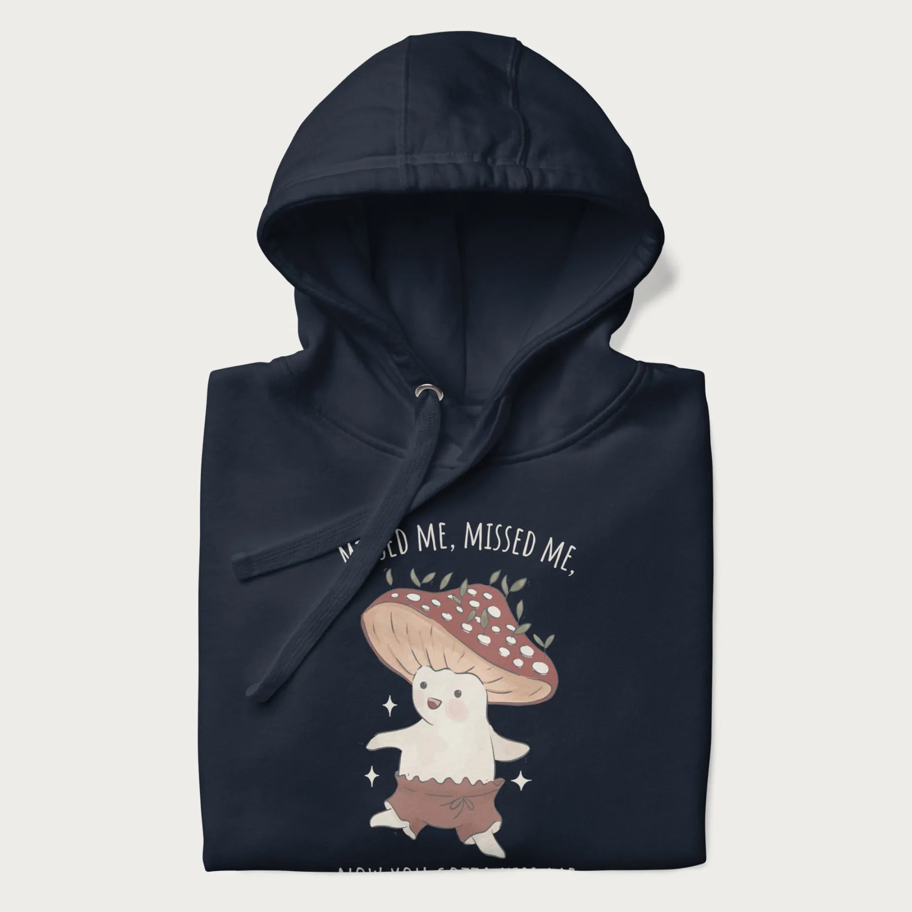 Folded navy blue hoodie with a graphic of a cute cottagecore mushroom character dancing and the phrase 'Missed Me, Missed Me, Now You Gotta Kiss Me'.