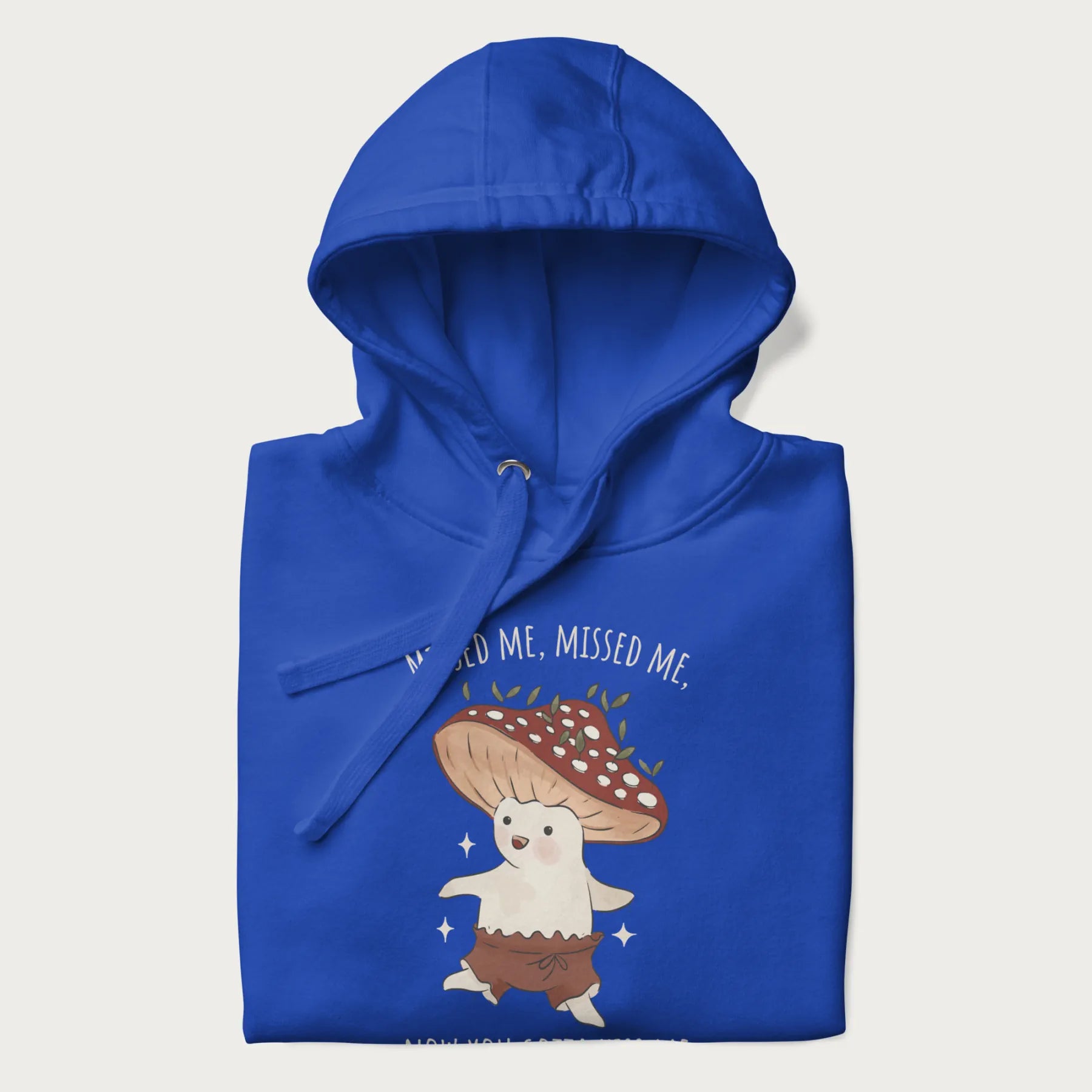 Folded royal blue hoodie with a graphic of a cute cottagecore mushroom character dancing and the phrase 'Missed Me, Missed Me, Now You Gotta Kiss Me'.