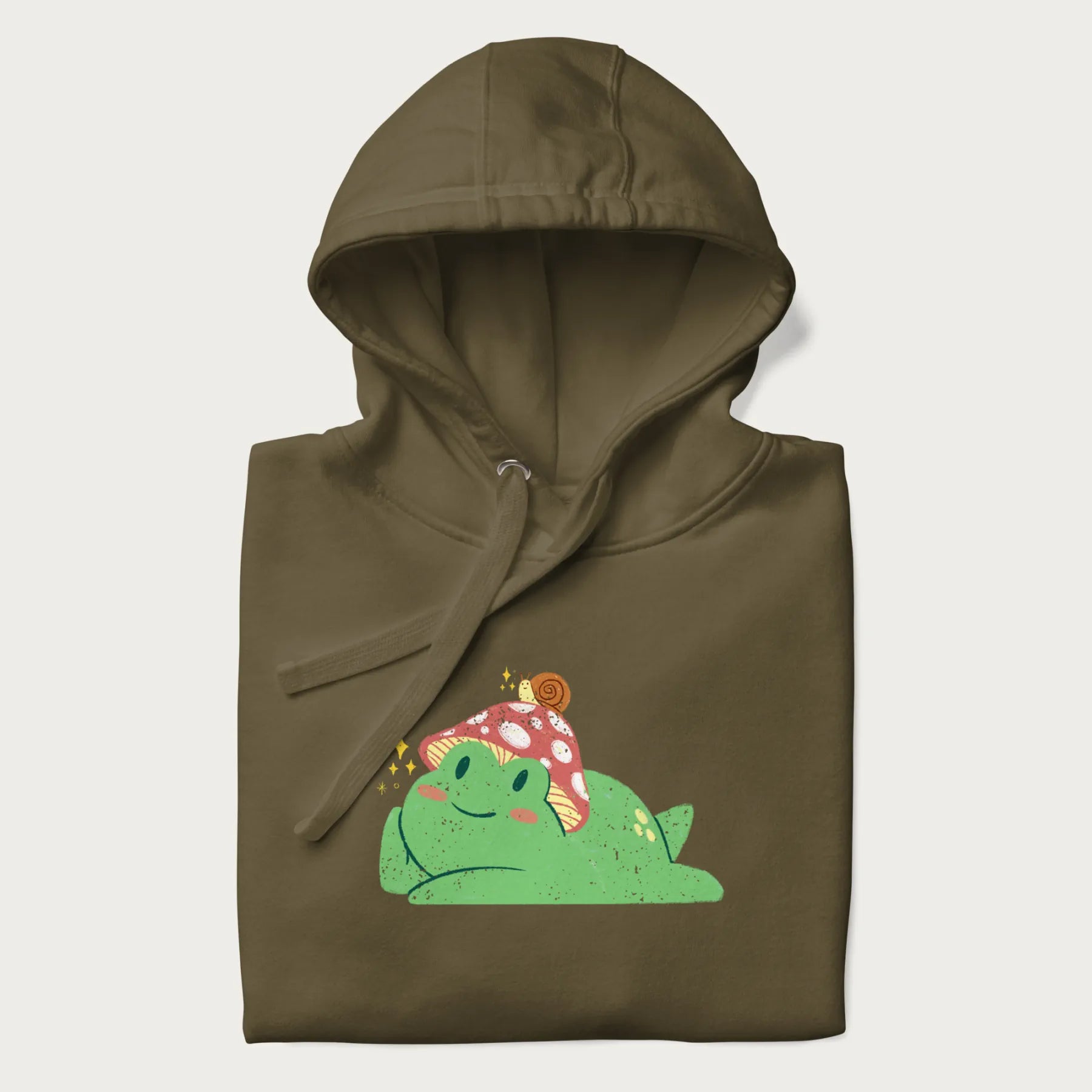Folded military green hoodie with a cottagecore design of a green frog wearing a mushroom cap and a snail on top.