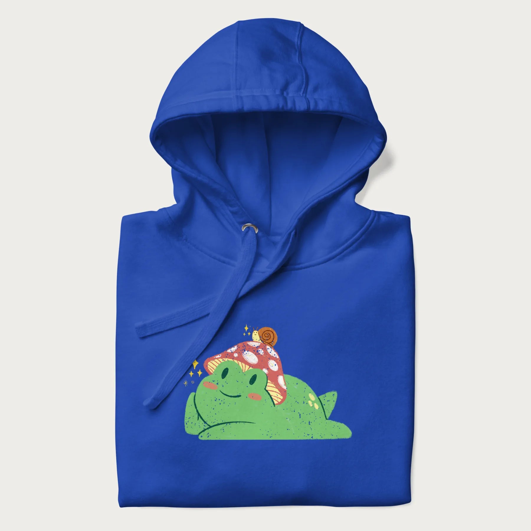 Folded royal blue hoodie with a cottagecore design of a green frog wearing a mushroom cap and a snail on top.