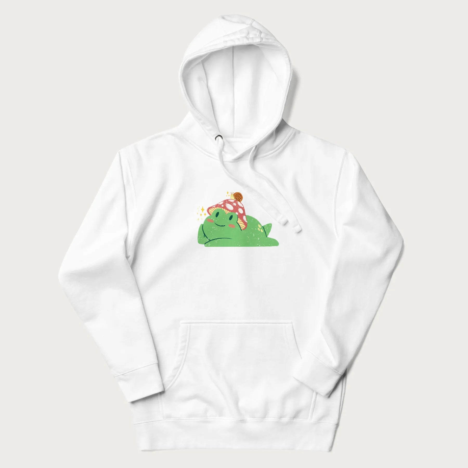 White hoodie with a cottagecore design of a green frog wearing a mushroom cap and a snail on top.