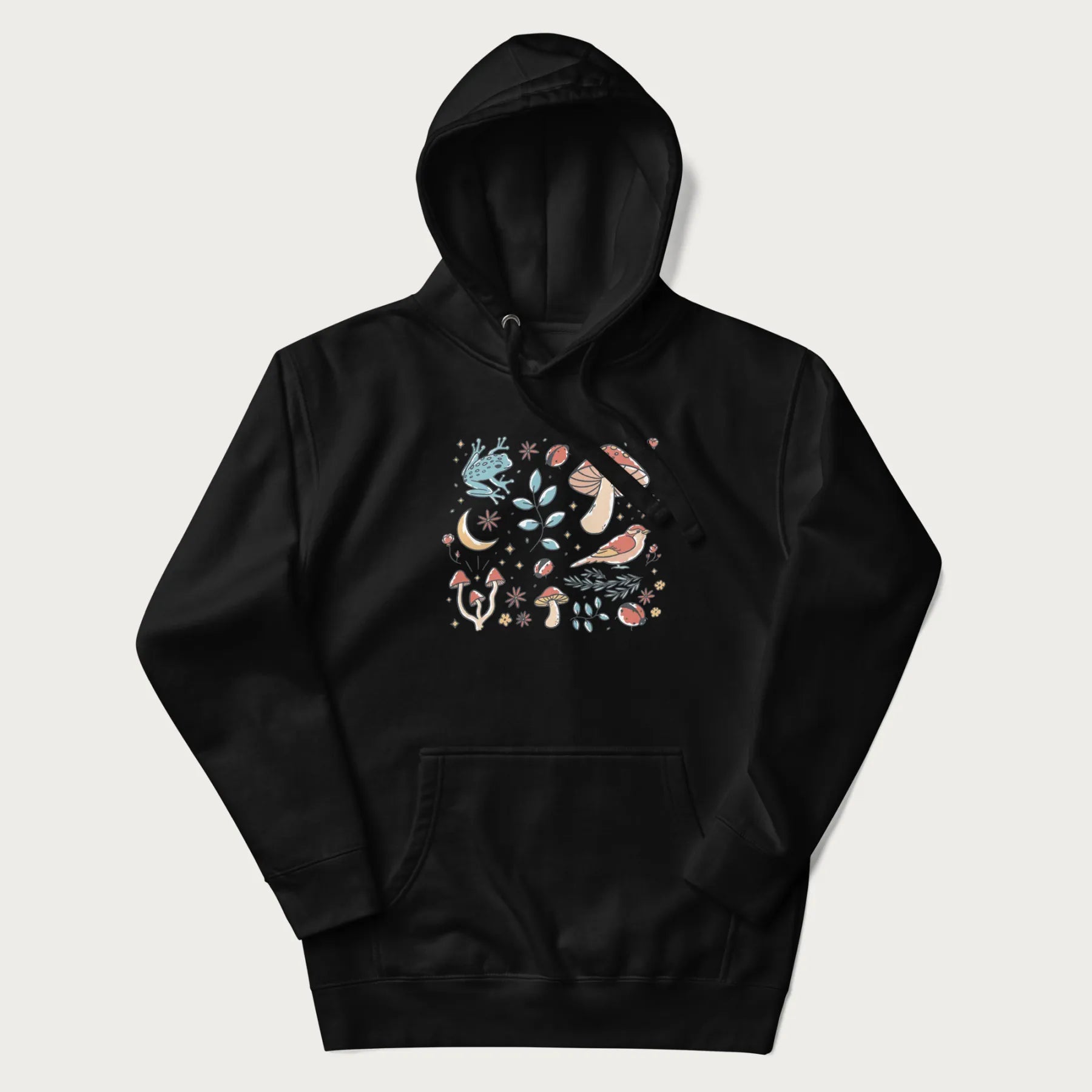 Black hoodie with a graphic of a blue frog, mushrooms, a bird, ladybugs, flowers, leaves, and a crescent moon.