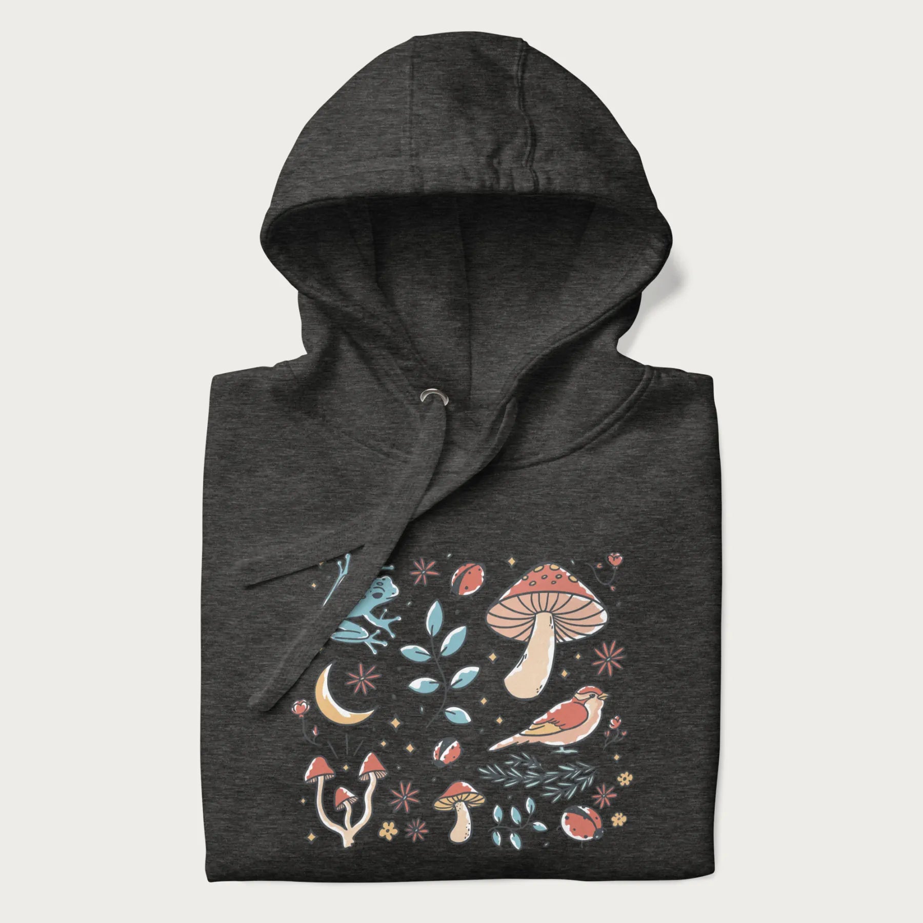 Folded dark grey hoodie with a graphic of a blue frog, mushrooms, a bird, ladybugs, flowers, leaves, and a crescent moon.