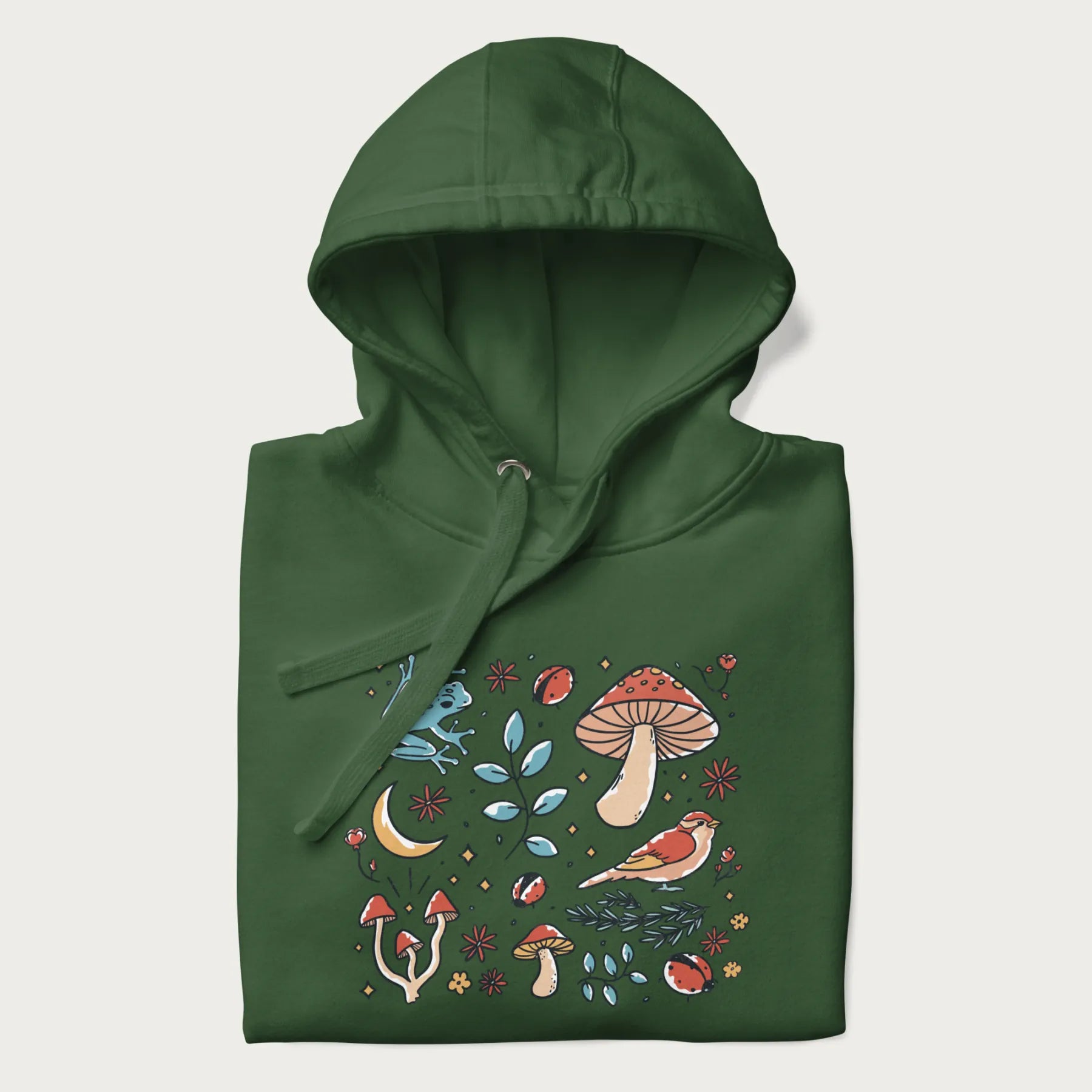 Folded forest green hoodie with a graphic of a blue frog, mushrooms, a bird, ladybugs, flowers, leaves, and a crescent moon.