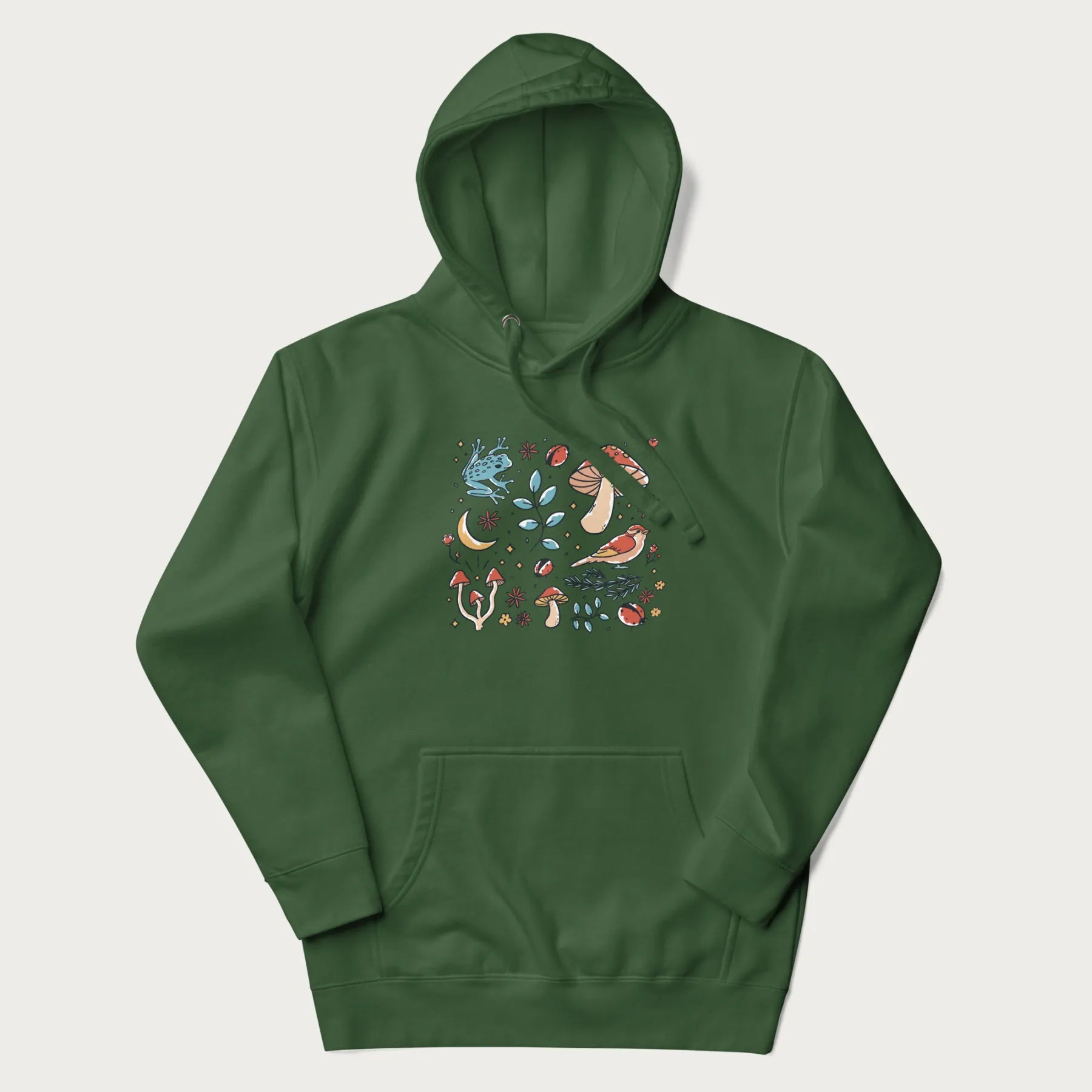 Forest green hoodie with a graphic of a blue frog, mushrooms, a bird, ladybugs, flowers, leaves, and a crescent moon.