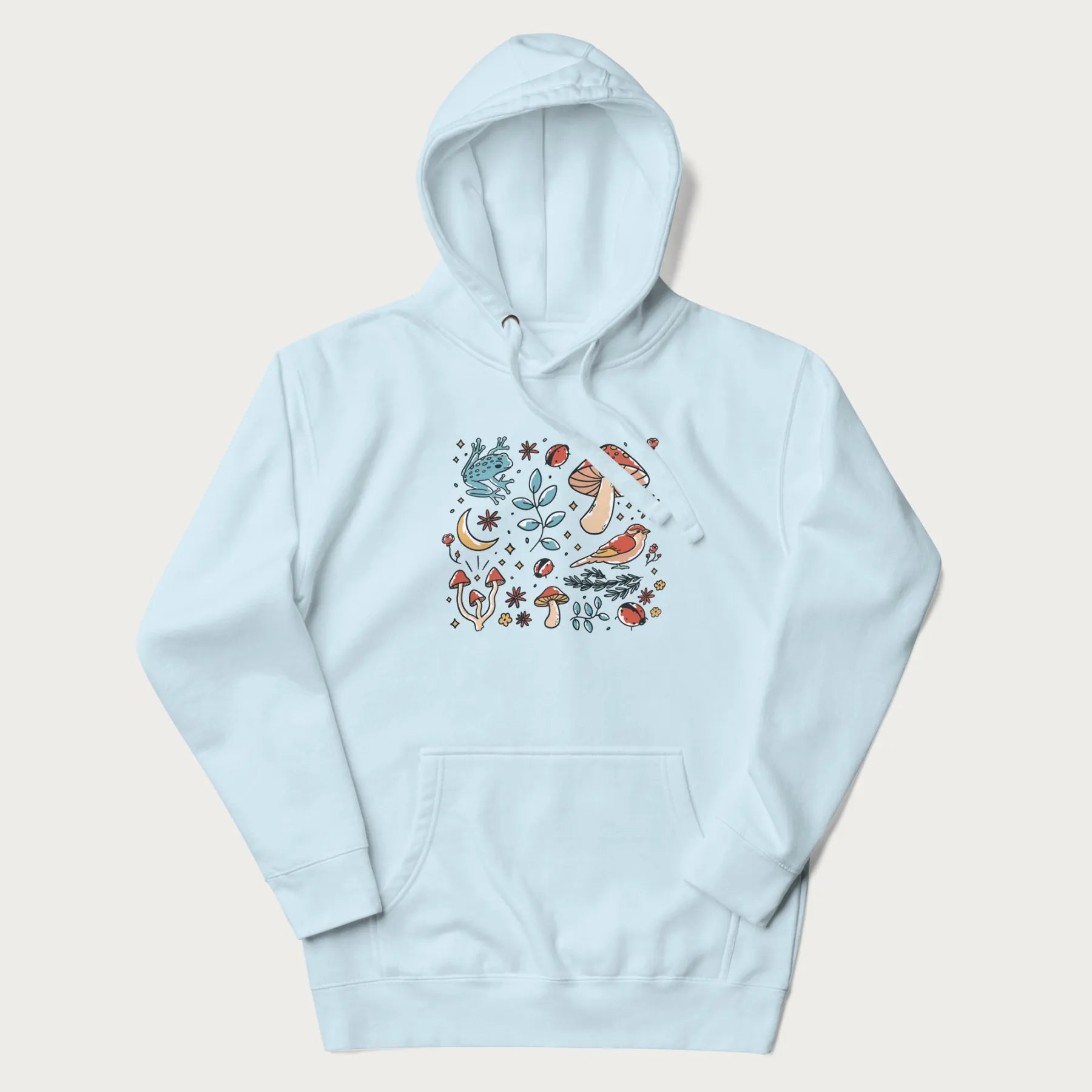 Light blue hoodie with a graphic of a blue frog, mushrooms, a bird, ladybugs, flowers, leaves, and a crescent moon.